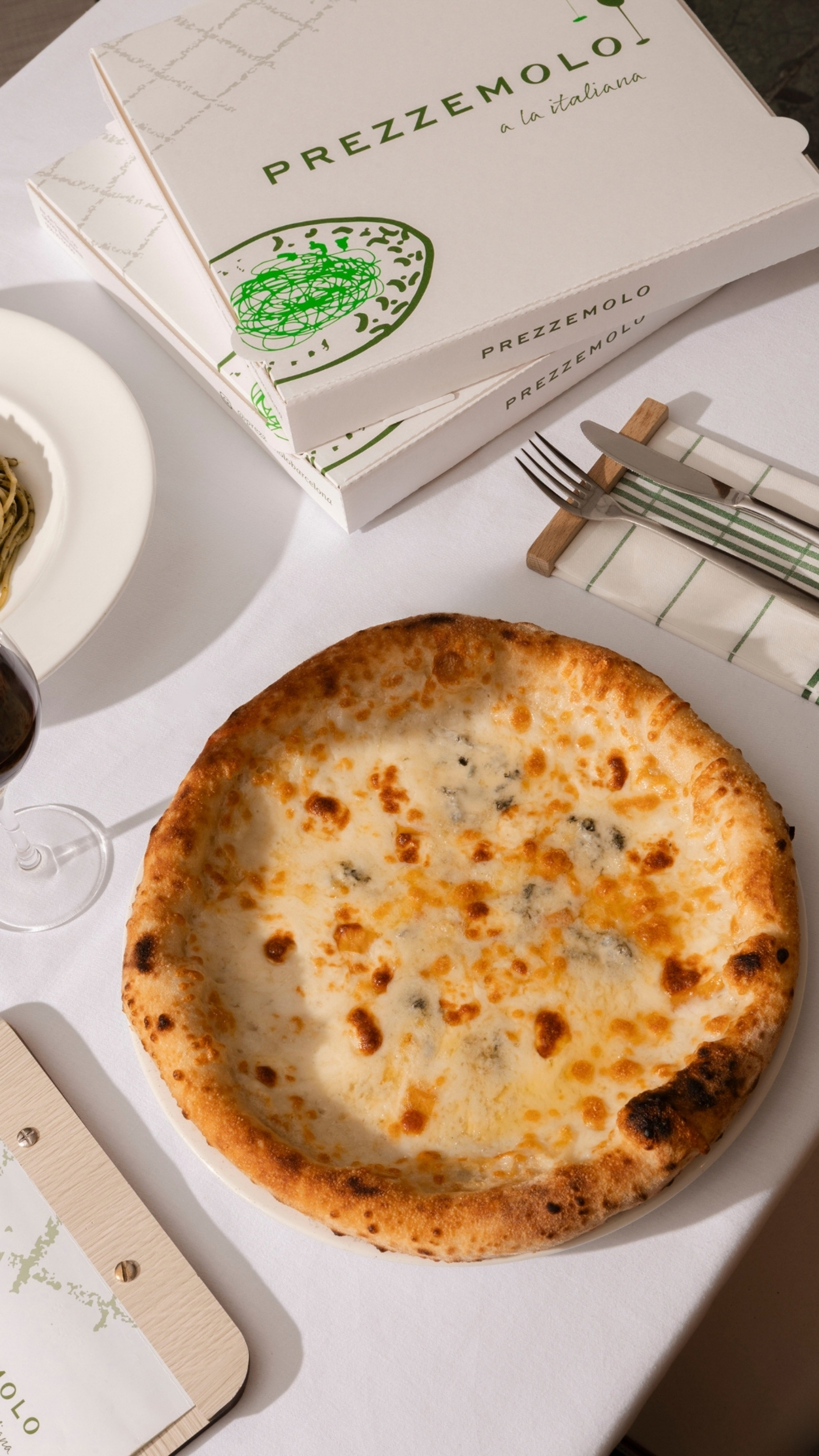 Prezzemolo quattro formaggi pizza, pasta, and wine on white table.