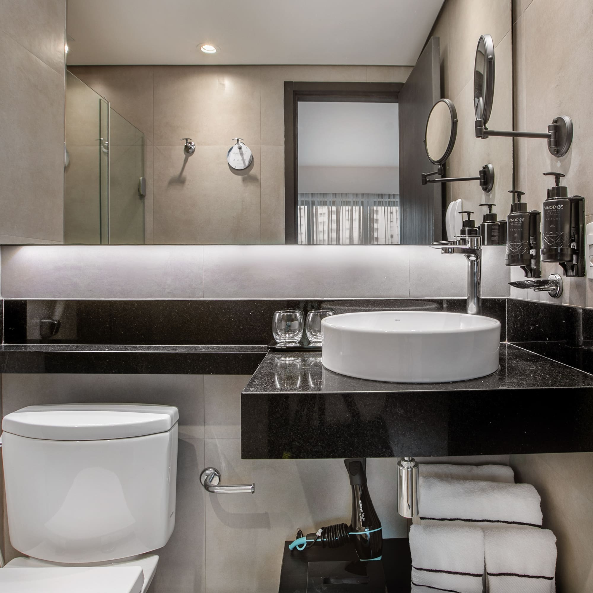 Modern hotel bathroom with a white vessel sink, black countertop, toilet, and lit mirror. - Deluxe Room Twin - Meliá Ibirapuera, São Paulo