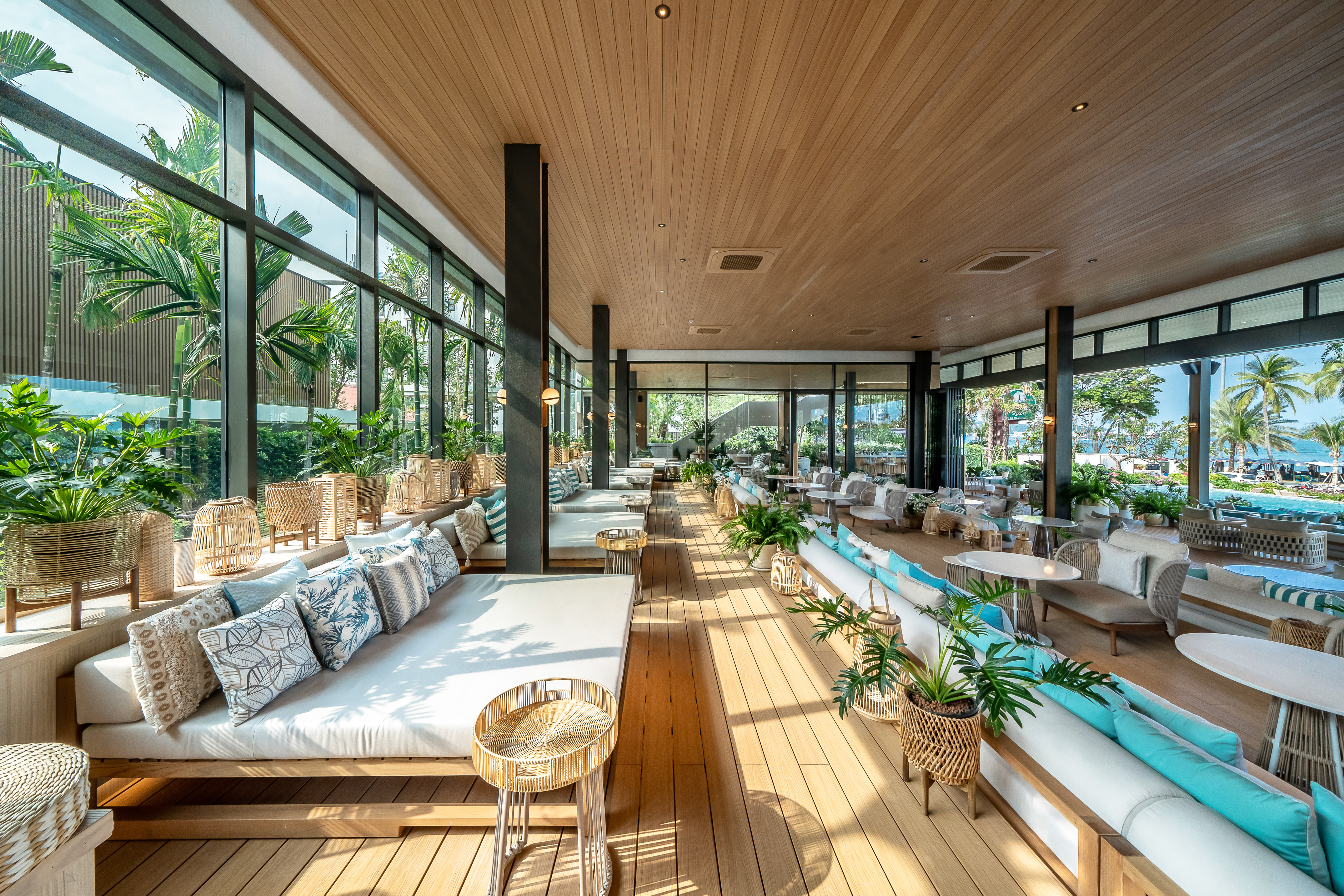 Modern resort lounge with daybeds, large windows, wood interior, and tropical view.