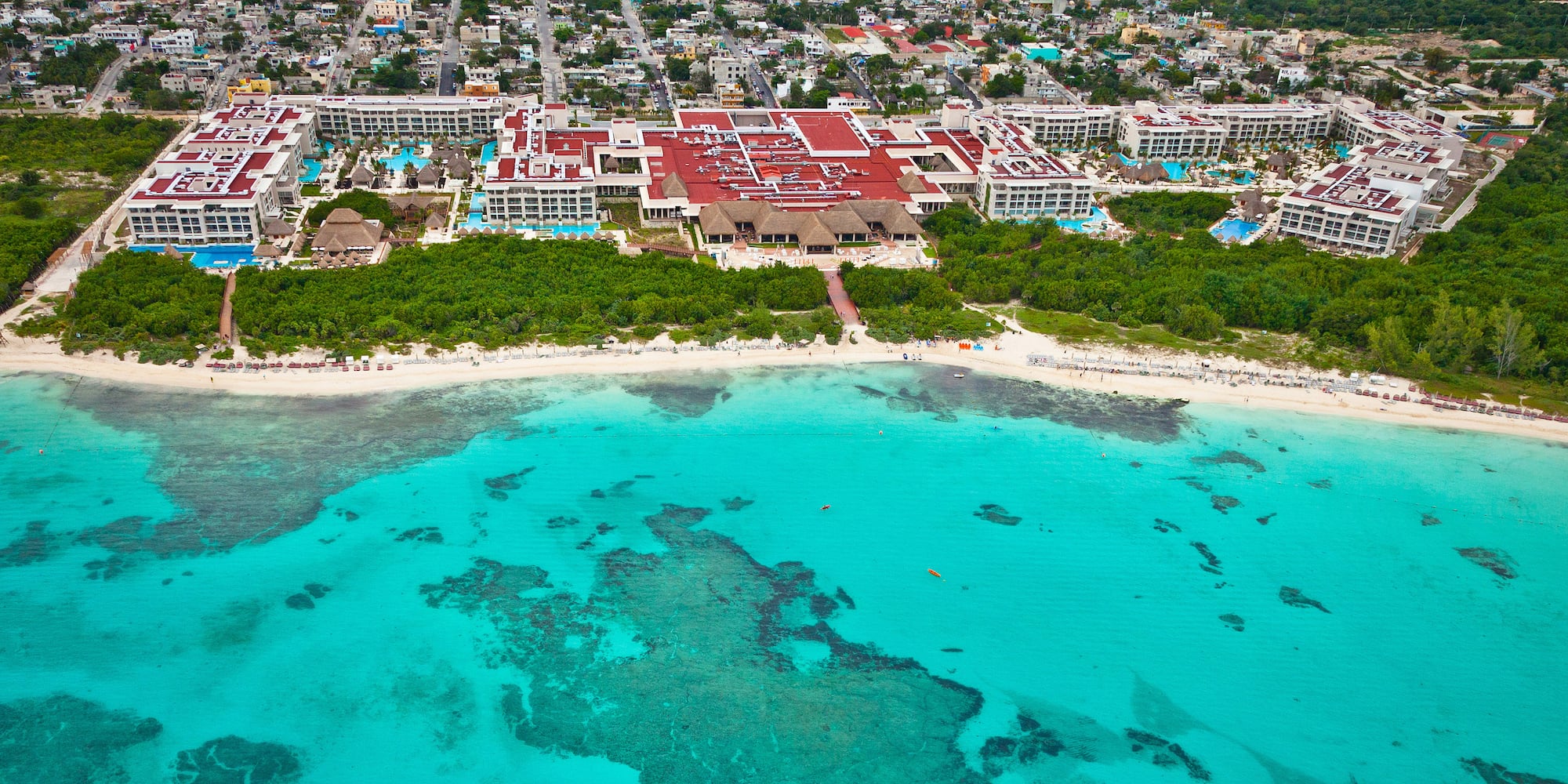 Luxury beachfront resort aerial view, red roofs, turquoise sea, white sand beach.