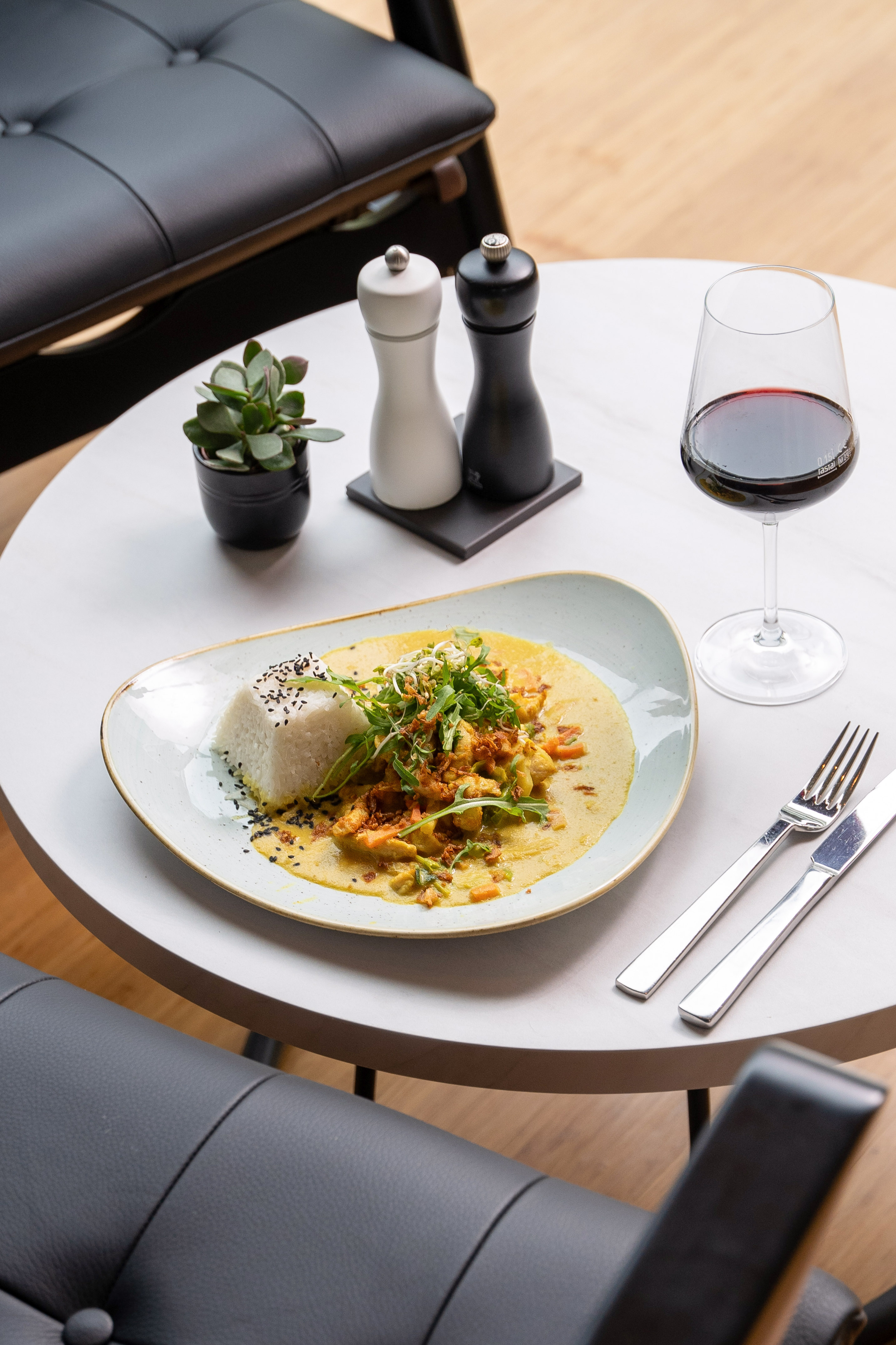 Yellow curry with rice, green garnish, wine, salt & pepper on white table.