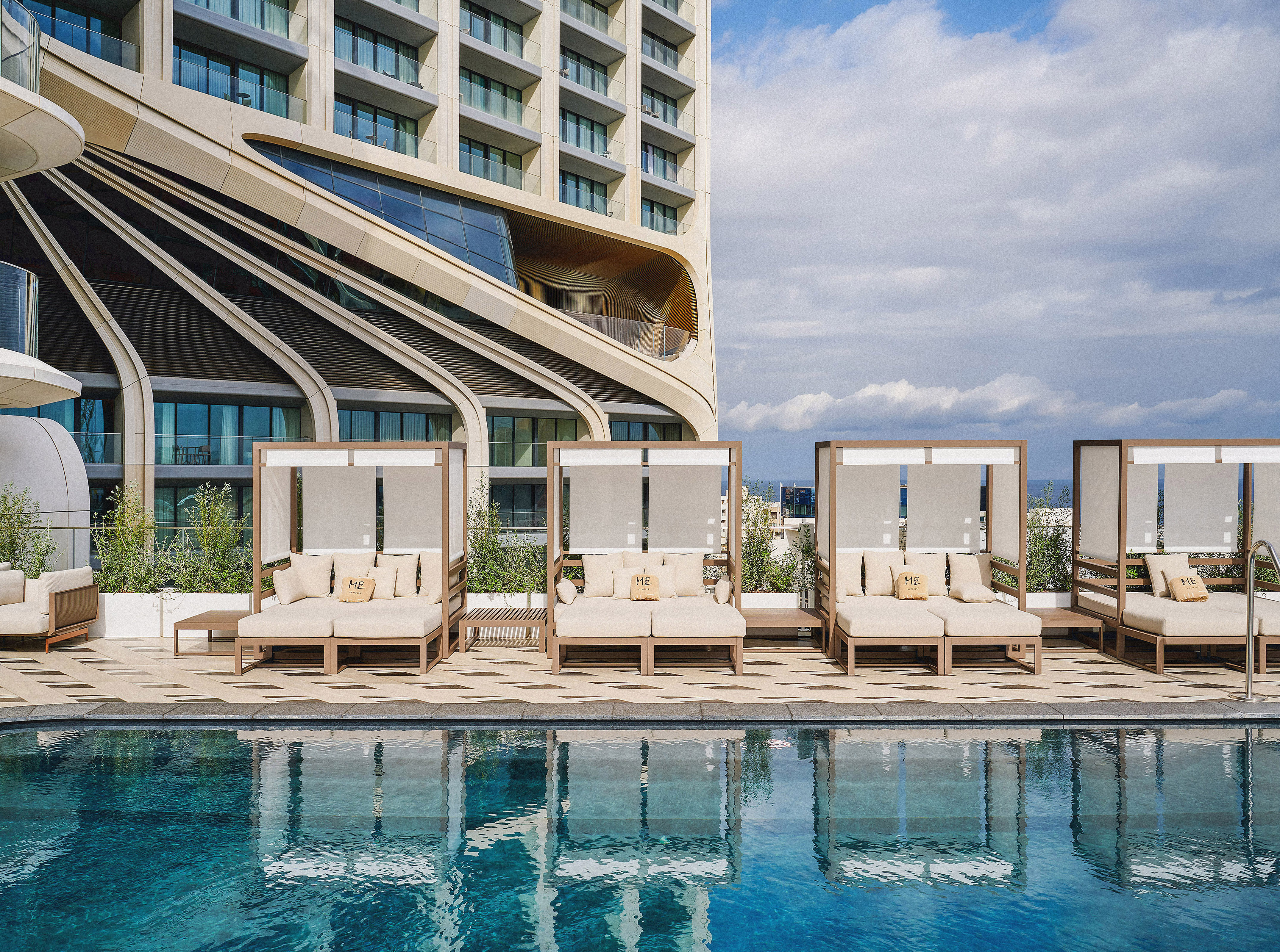 ME hotel rooftop pool with luxury daybeds and modern building architecture.
