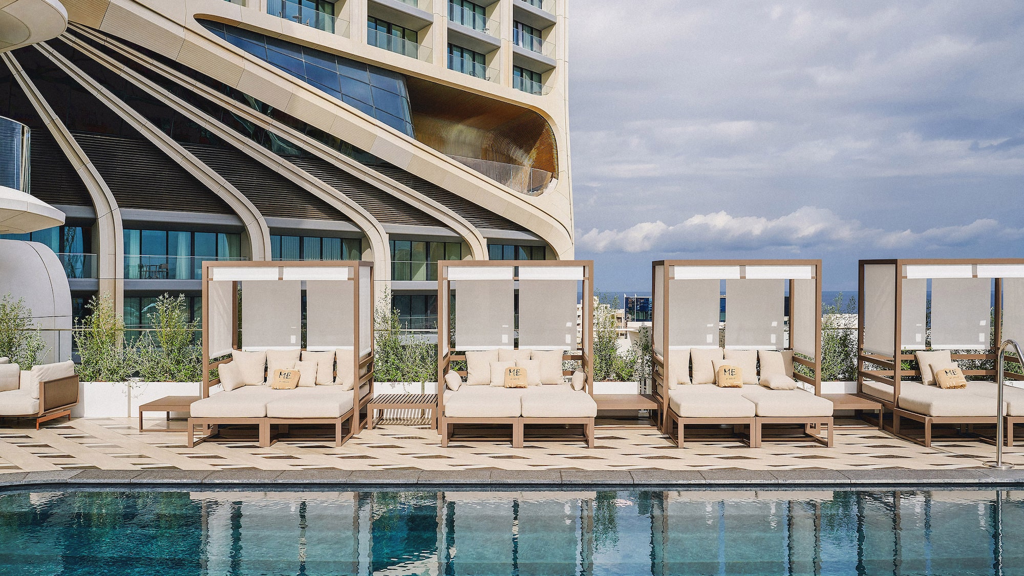 ME hotel rooftop pool with luxury daybeds and modern building architecture.