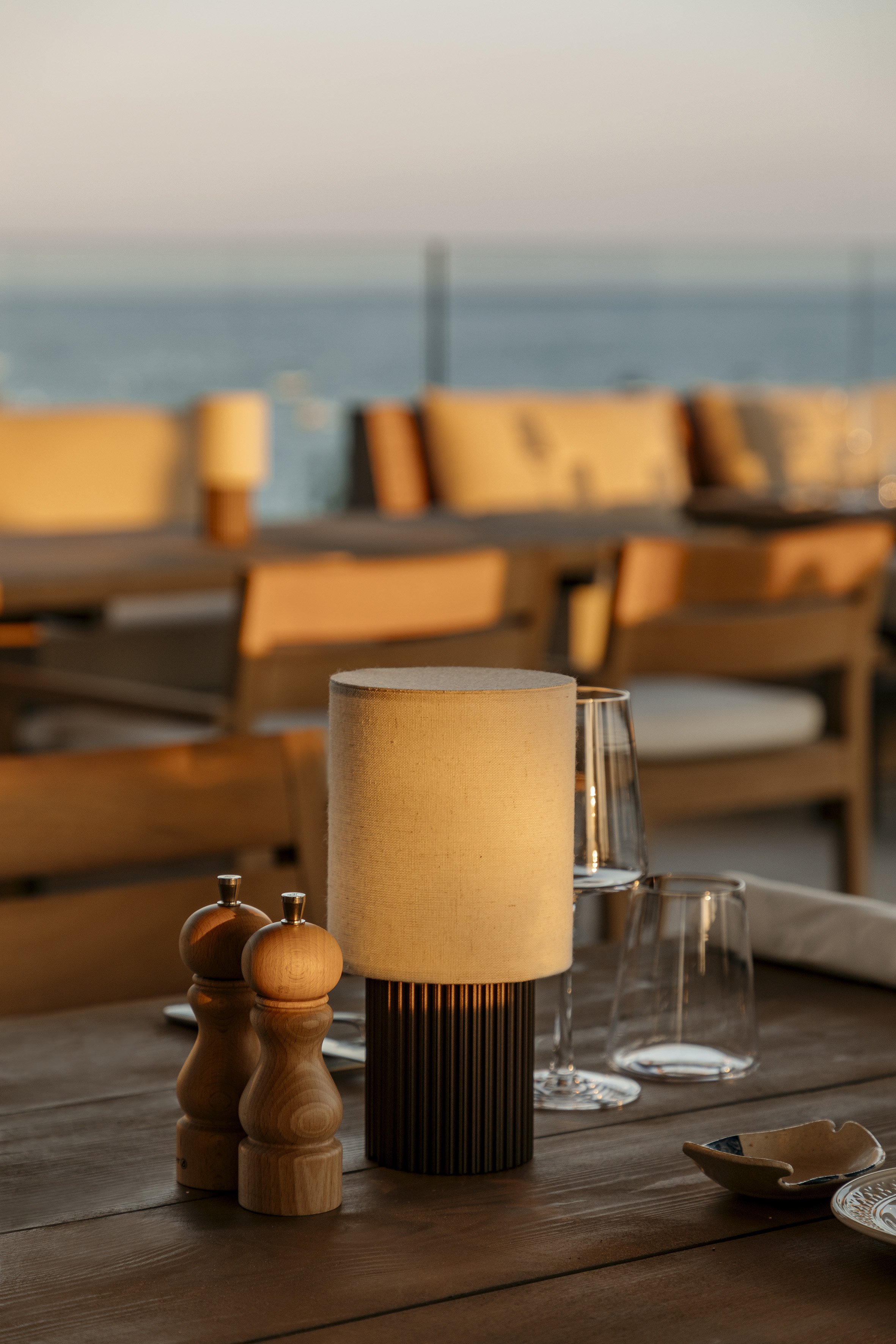 Seaside restaurant table with lamp, shakers, glasses, and sunset glow.