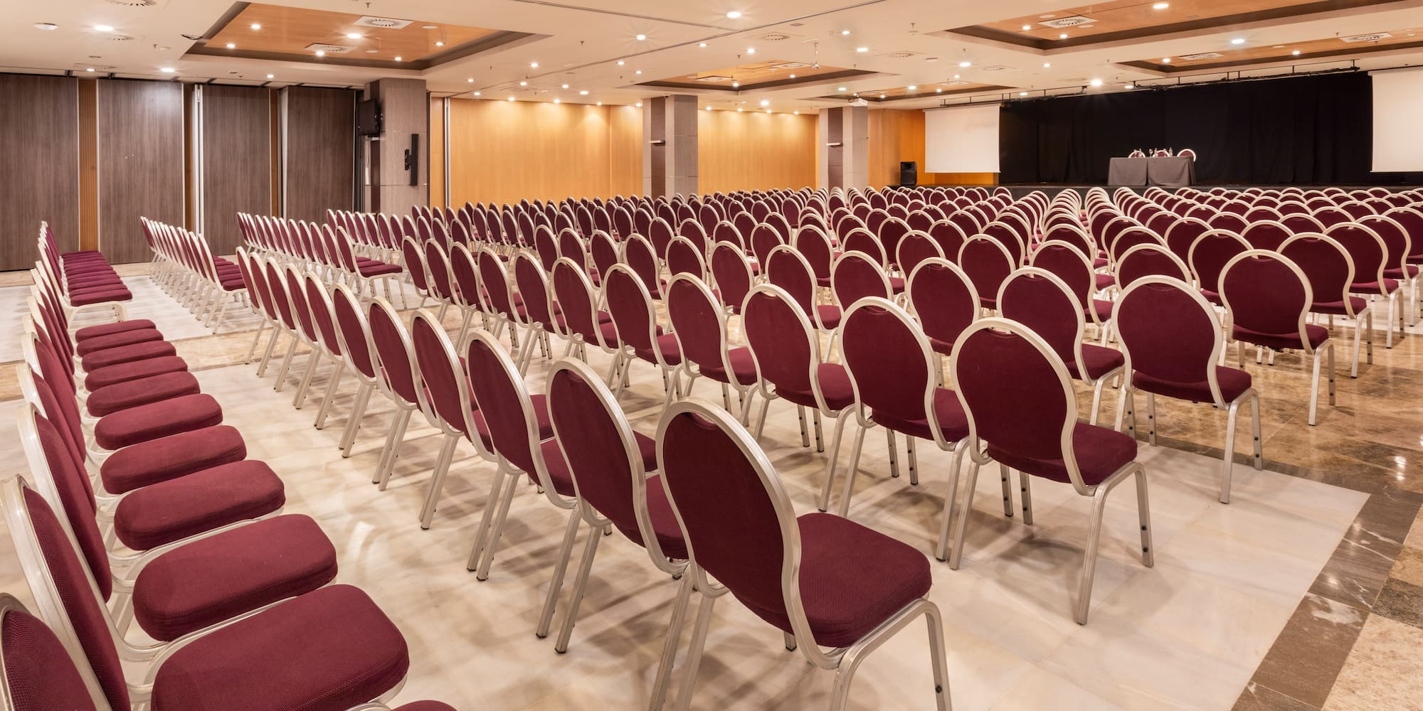 Empty conference room with rows of burgundy chairs and presentation stage.