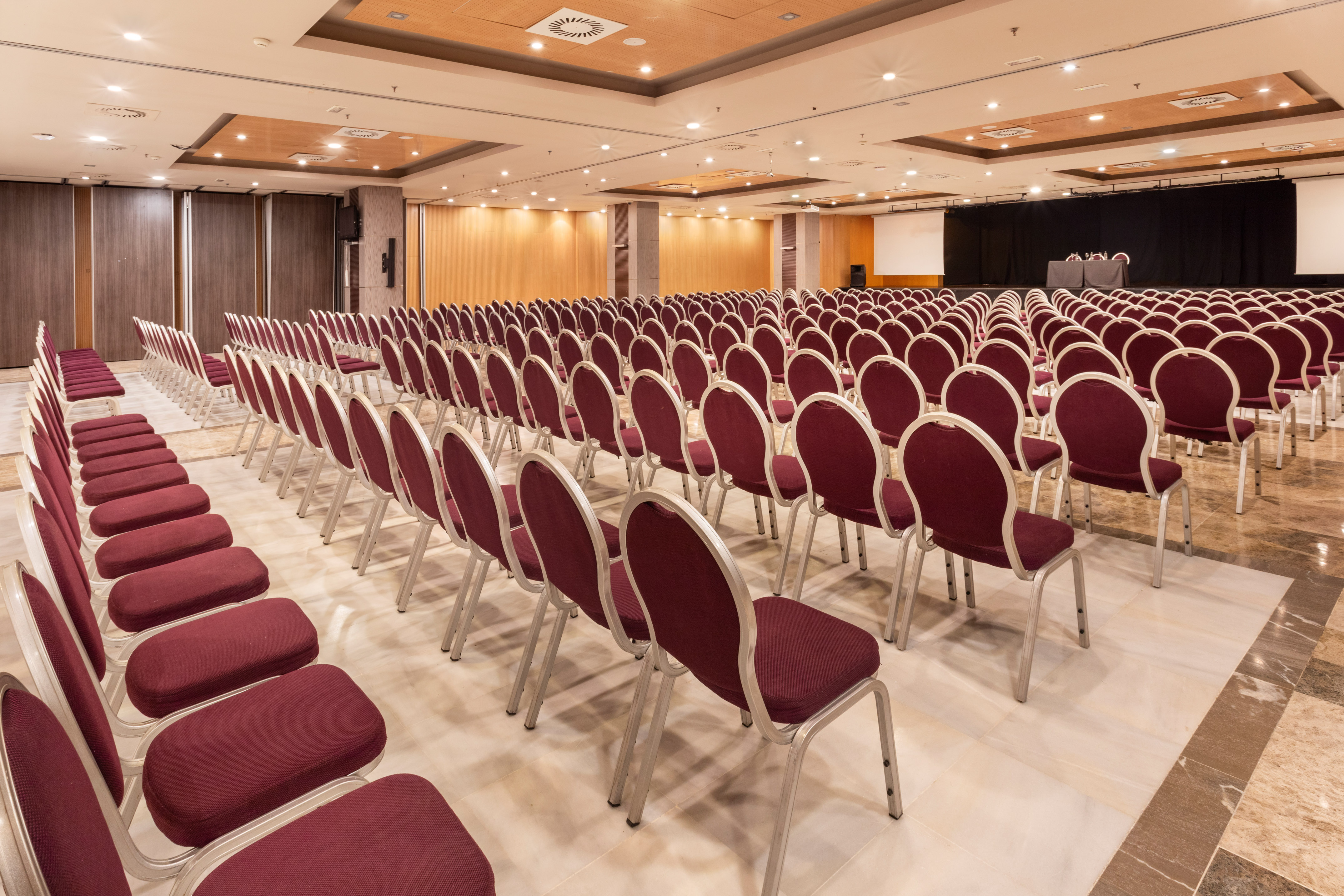 Empty conference room with rows of burgundy chairs and presentation stage.