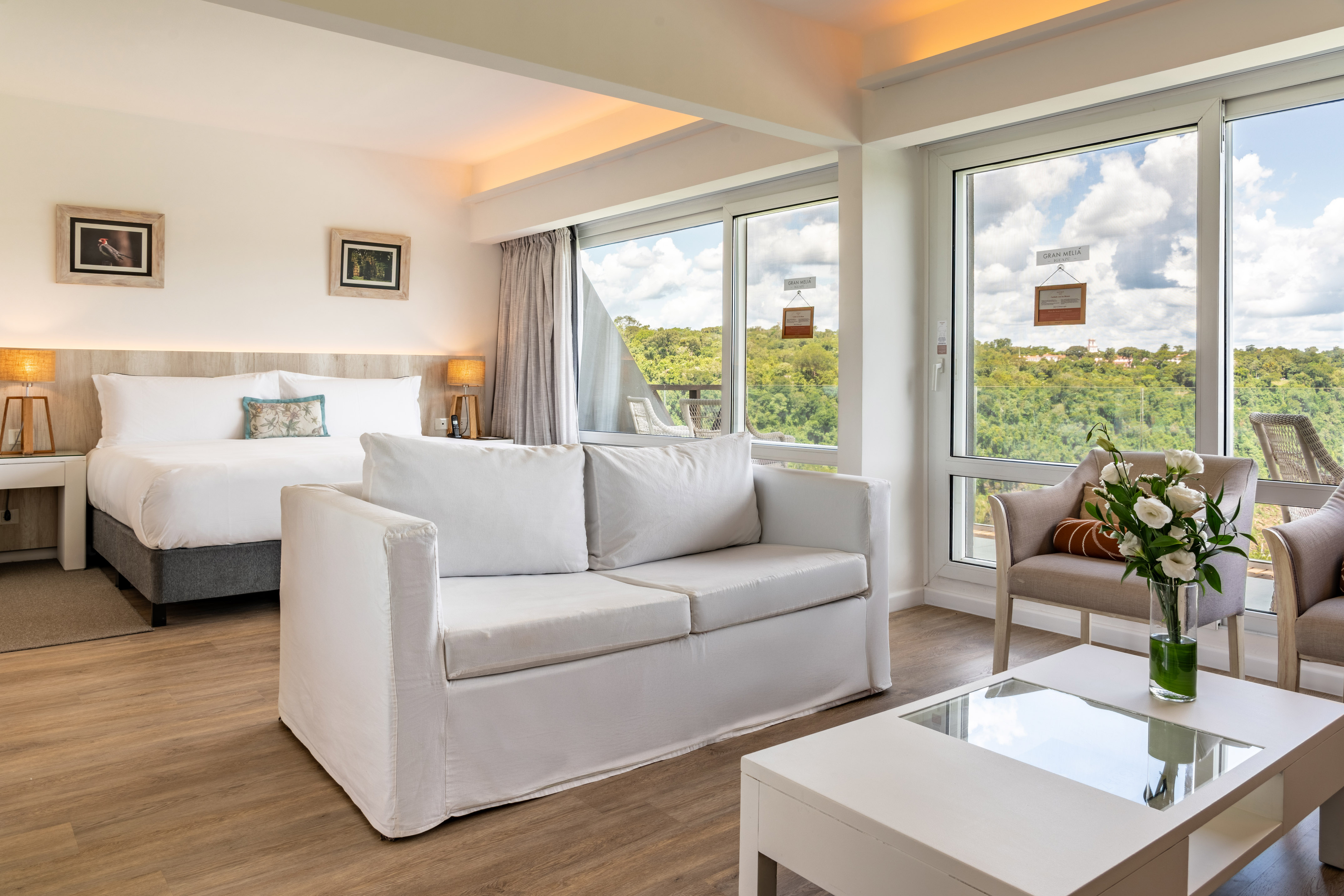 Modern hotel suite with king bed, white sofa, and scenic forest view.