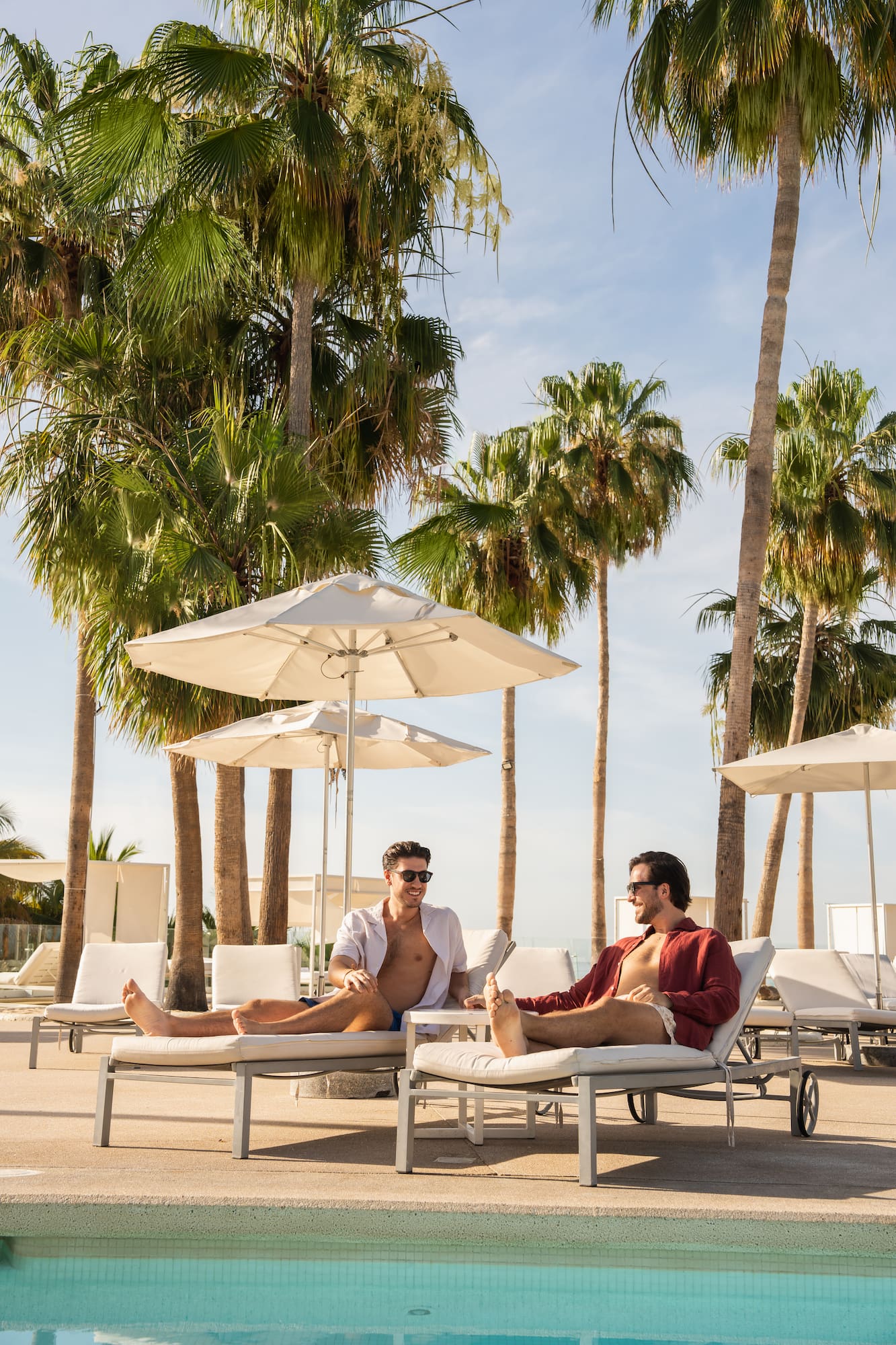 two men sitting on lounge chairs under umbrellas