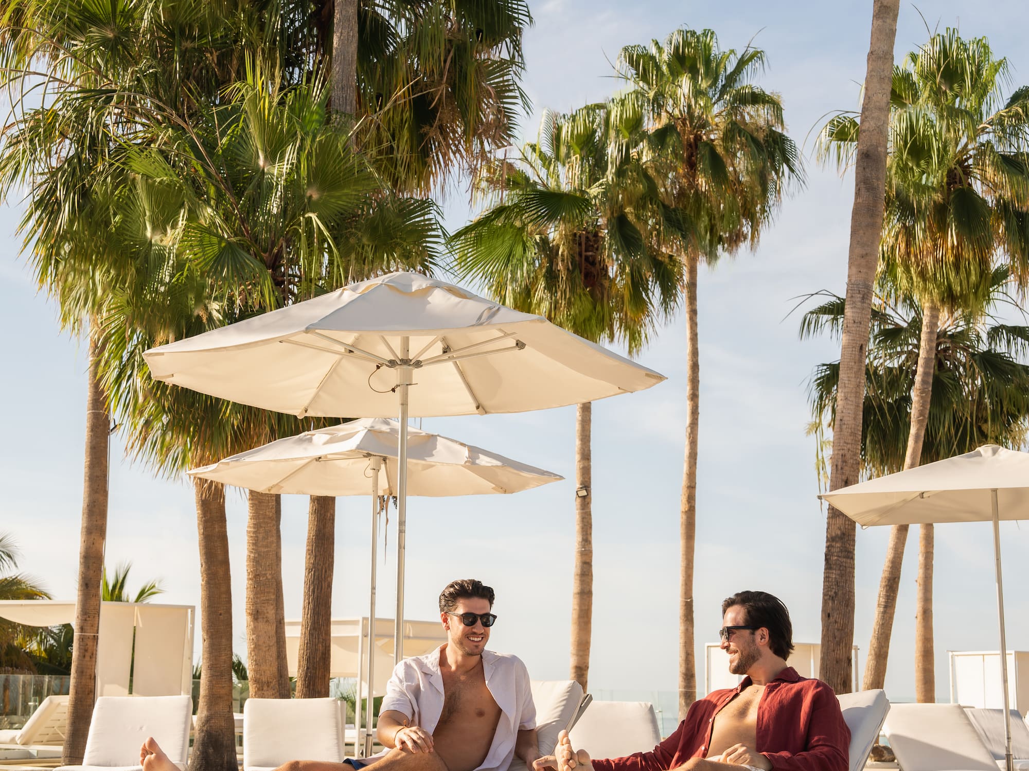 two men sitting on lounge chairs under umbrellas