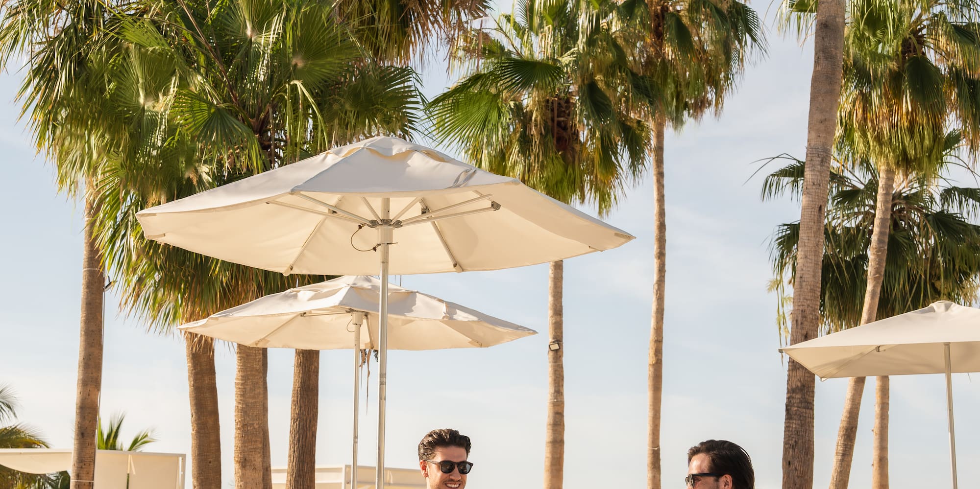 two men sitting on lounge chairs under umbrellas