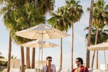 two men sitting on lounge chairs under umbrellas