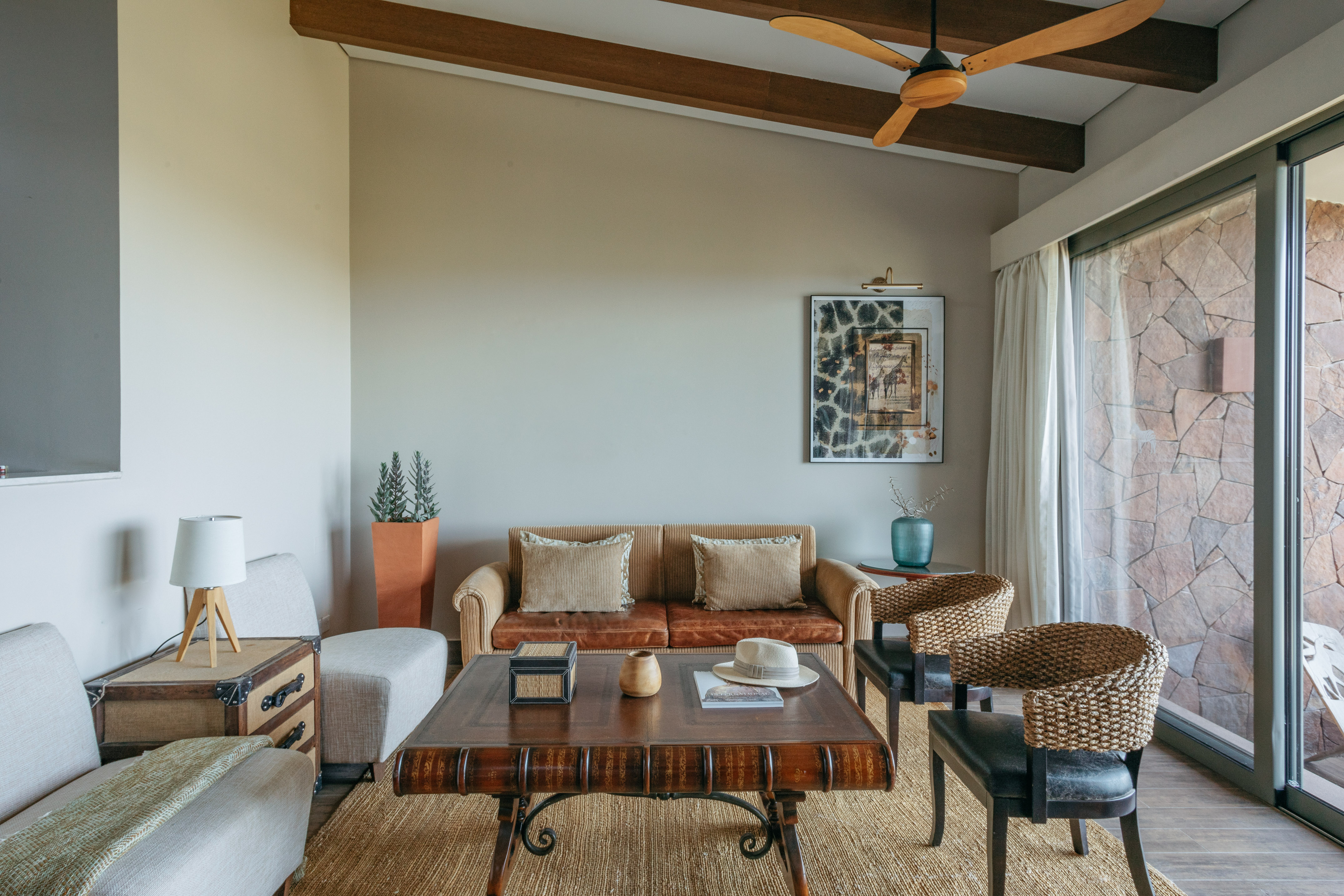 Safari living room with leather sofa, rustic decor, woven chairs, wood fan.