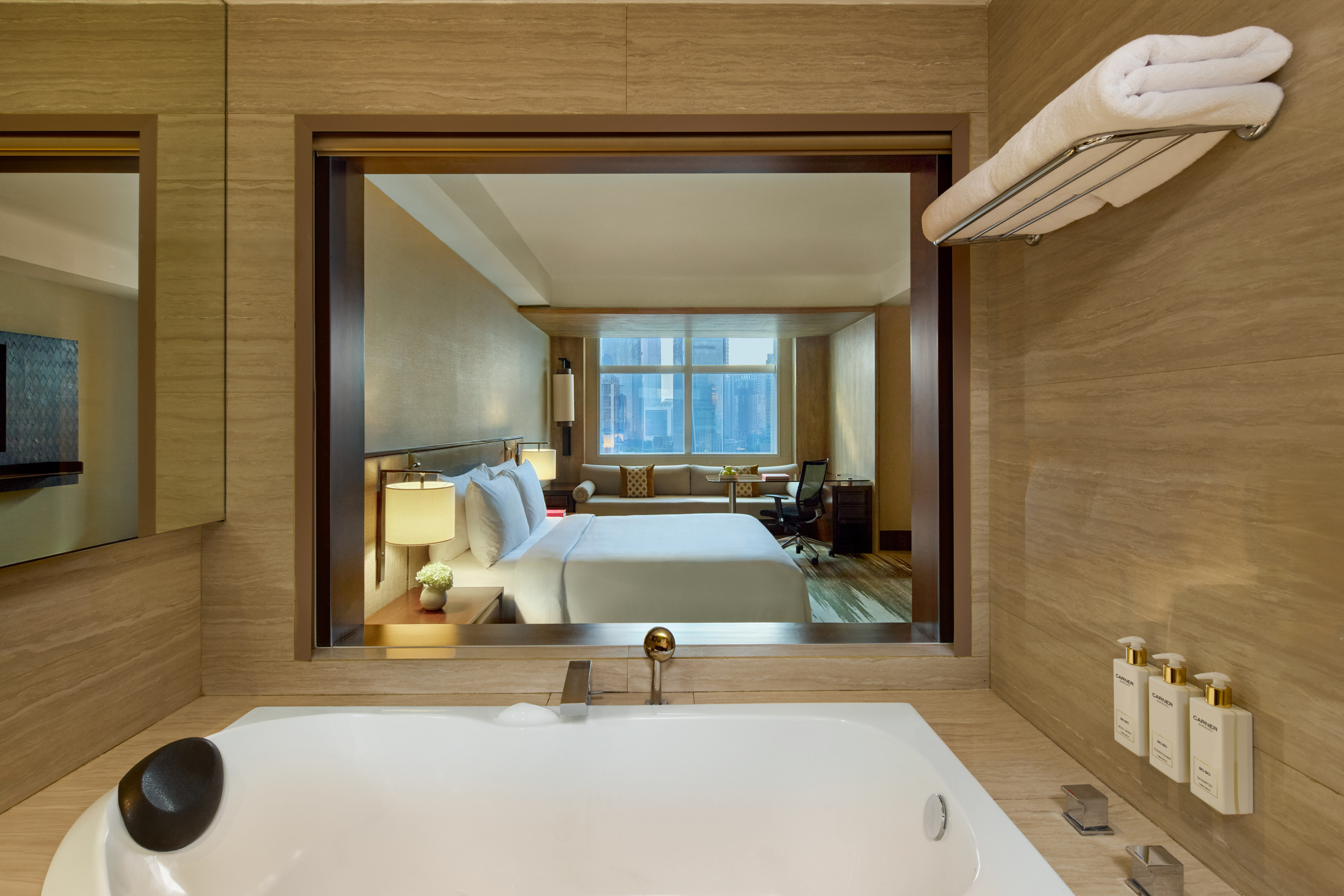 Luxury hotel suite with bathtub and bedroom overlooking city view.