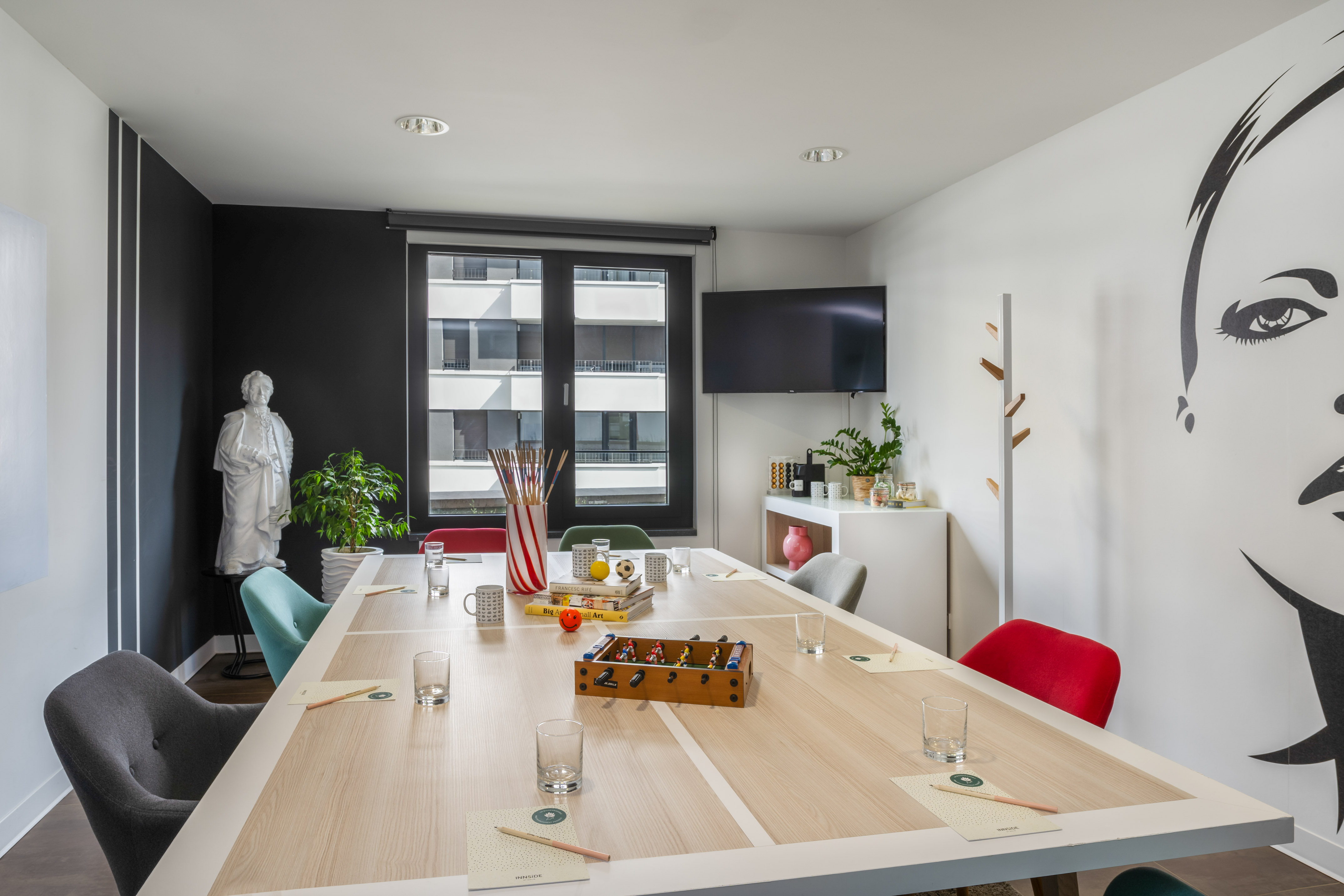 Modern meeting room with colorful chairs, foosball table, TV, and wall art.