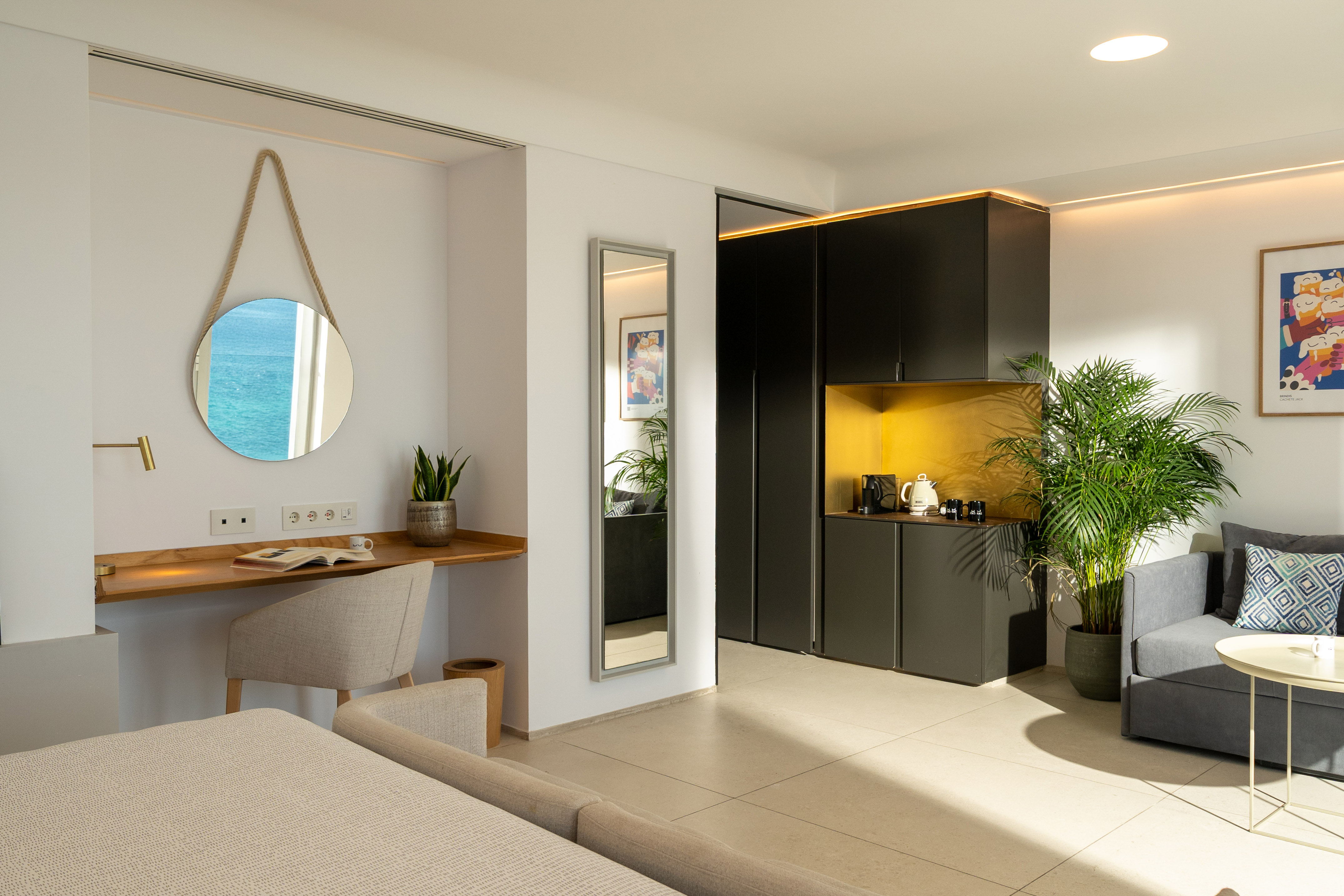Modern hotel suite with ocean view mirror, desk, kitchenette, and living area.