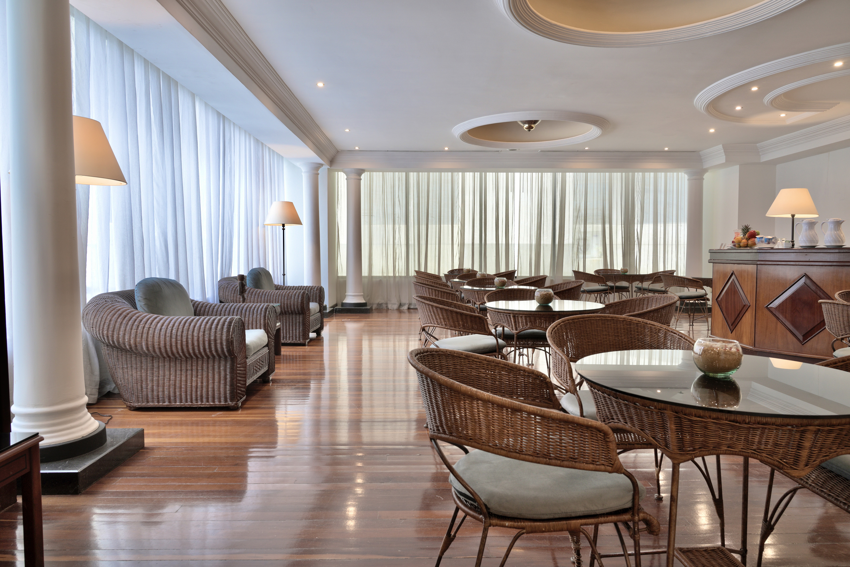 Bright resort lounge with rattan chairs, glass tables, polished wood floor.