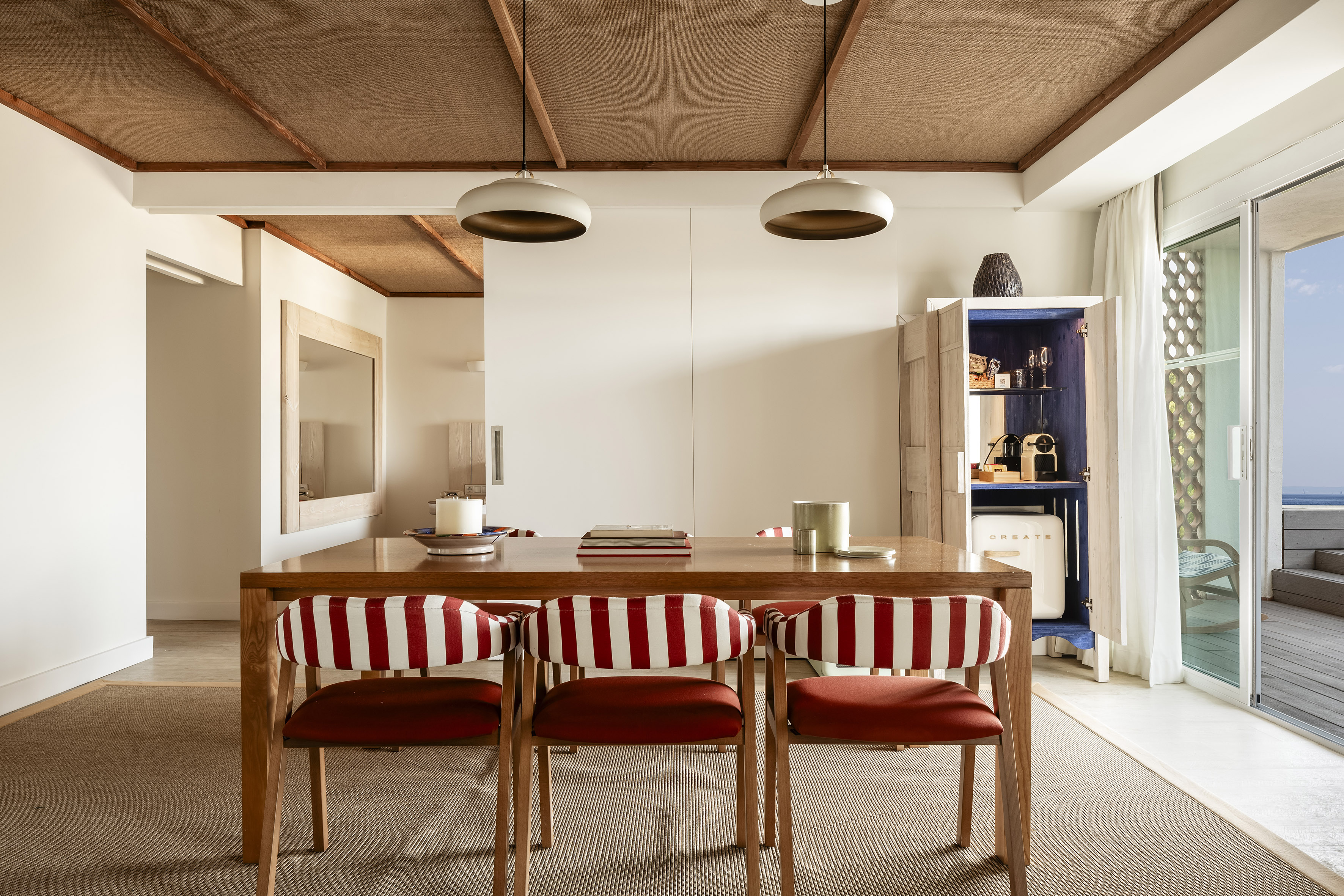 Coastal dining room with wood table, red striped chairs, and ocean view patio.