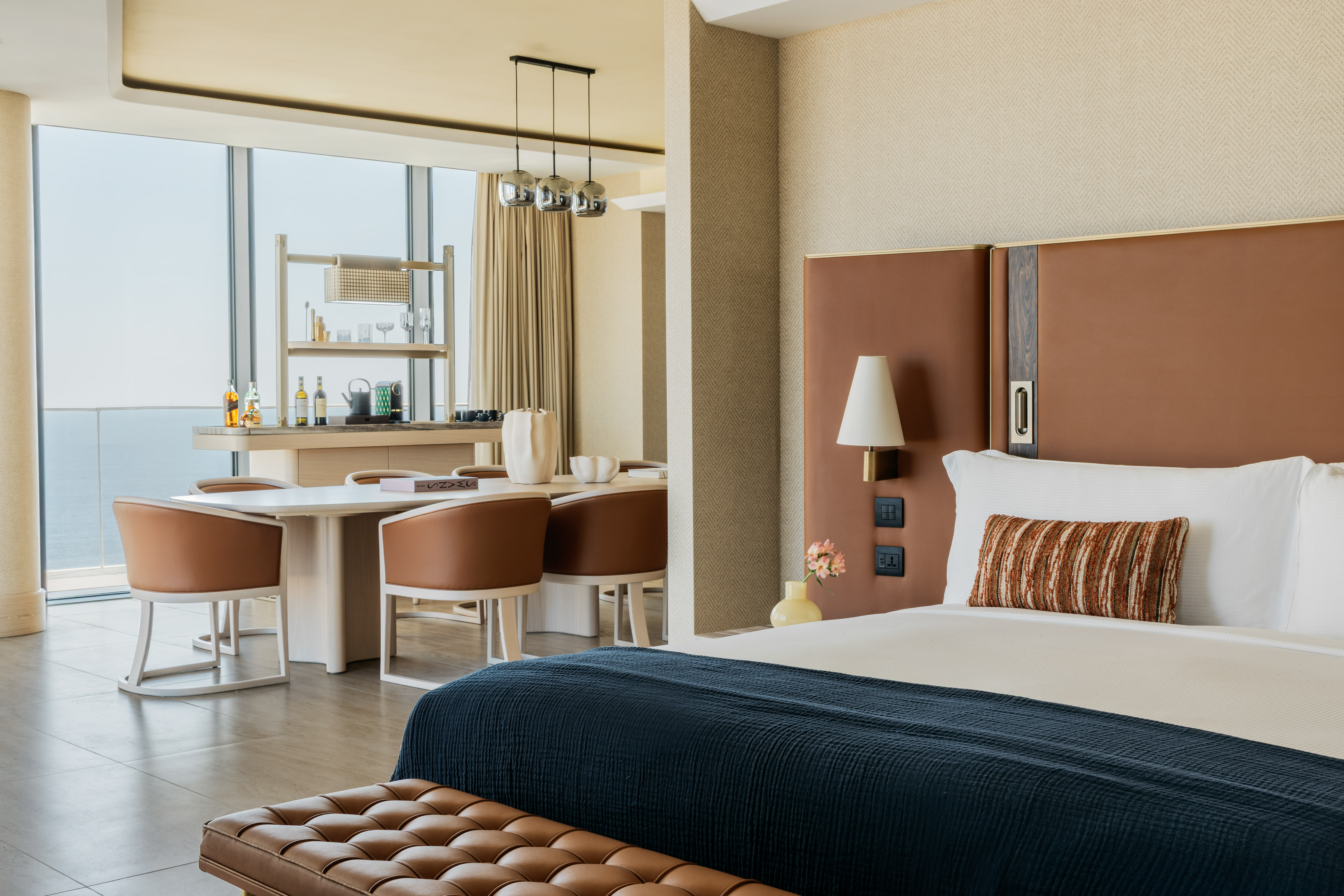 Modern luxury hotel suite with bedroom, dining area, and panoramic ocean views.
