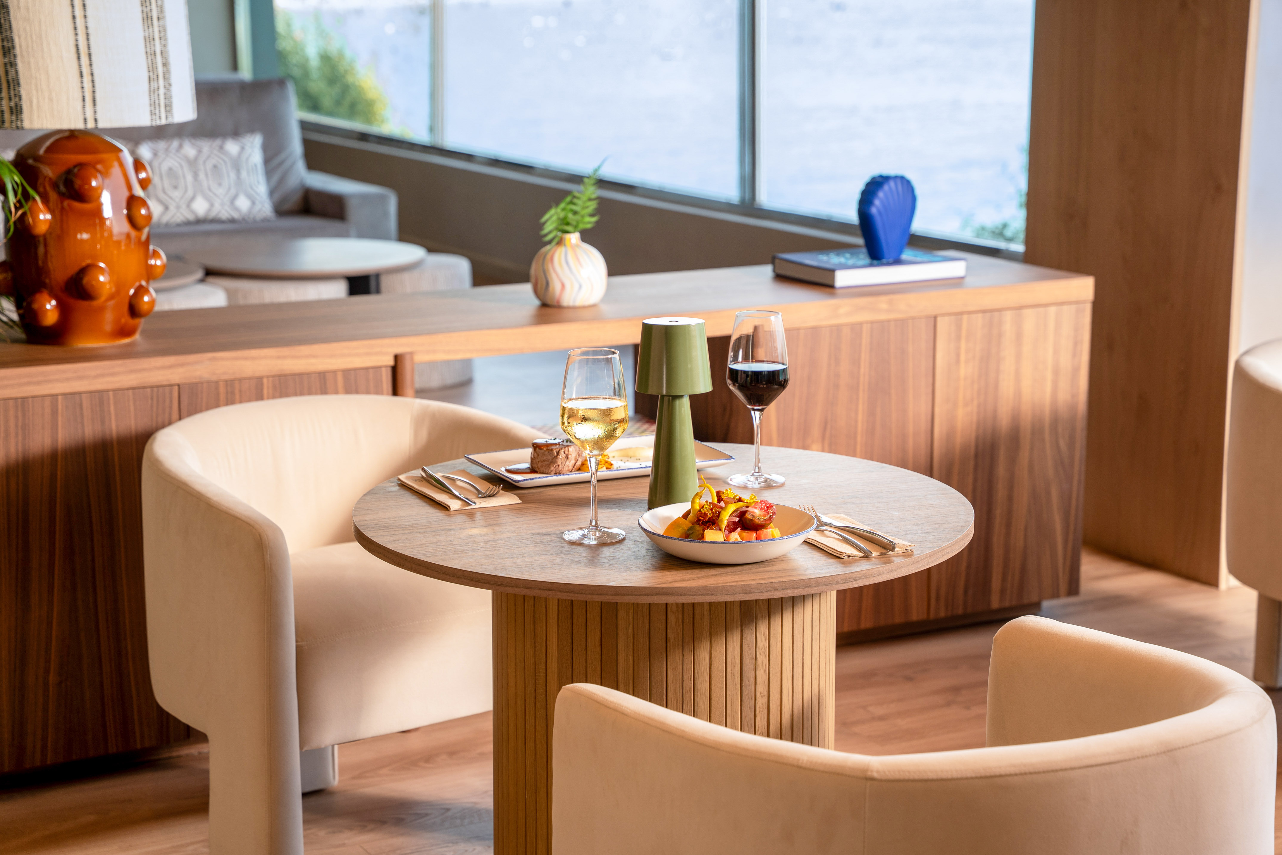 Modern dining table with wine, small plates, and elegant decor overlooking water.