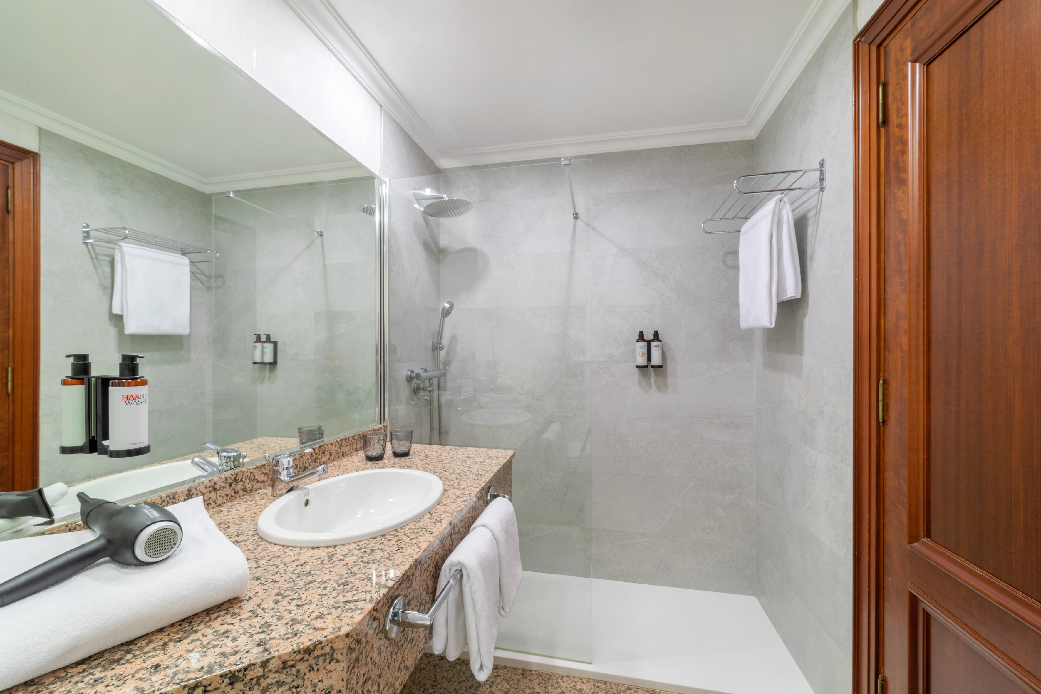 Clean modern bathroom with walk-in shower, granite vanity, and hairdryer.