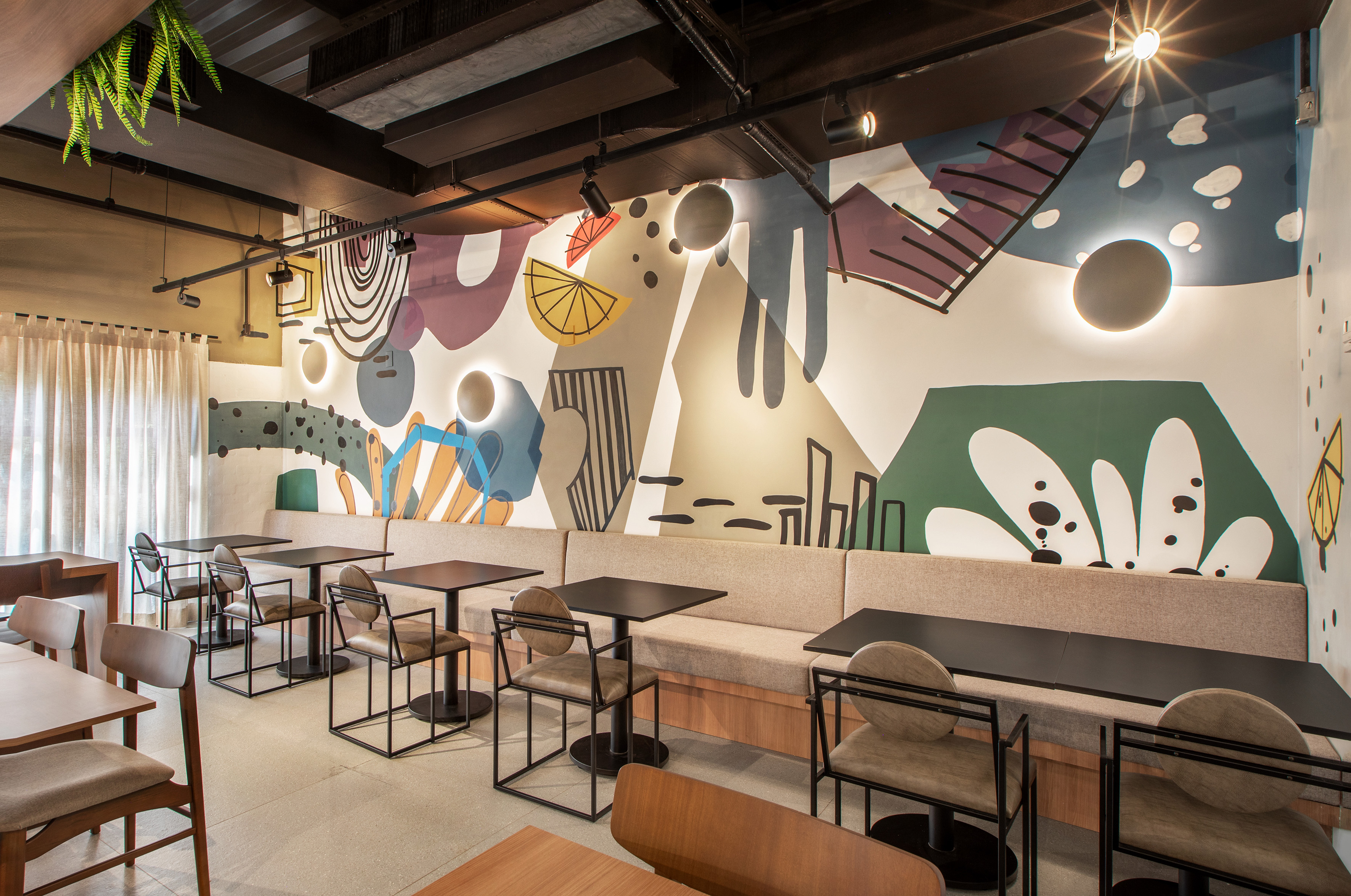 Modern cafe interior with abstract mural, track lighting, and dining tables.