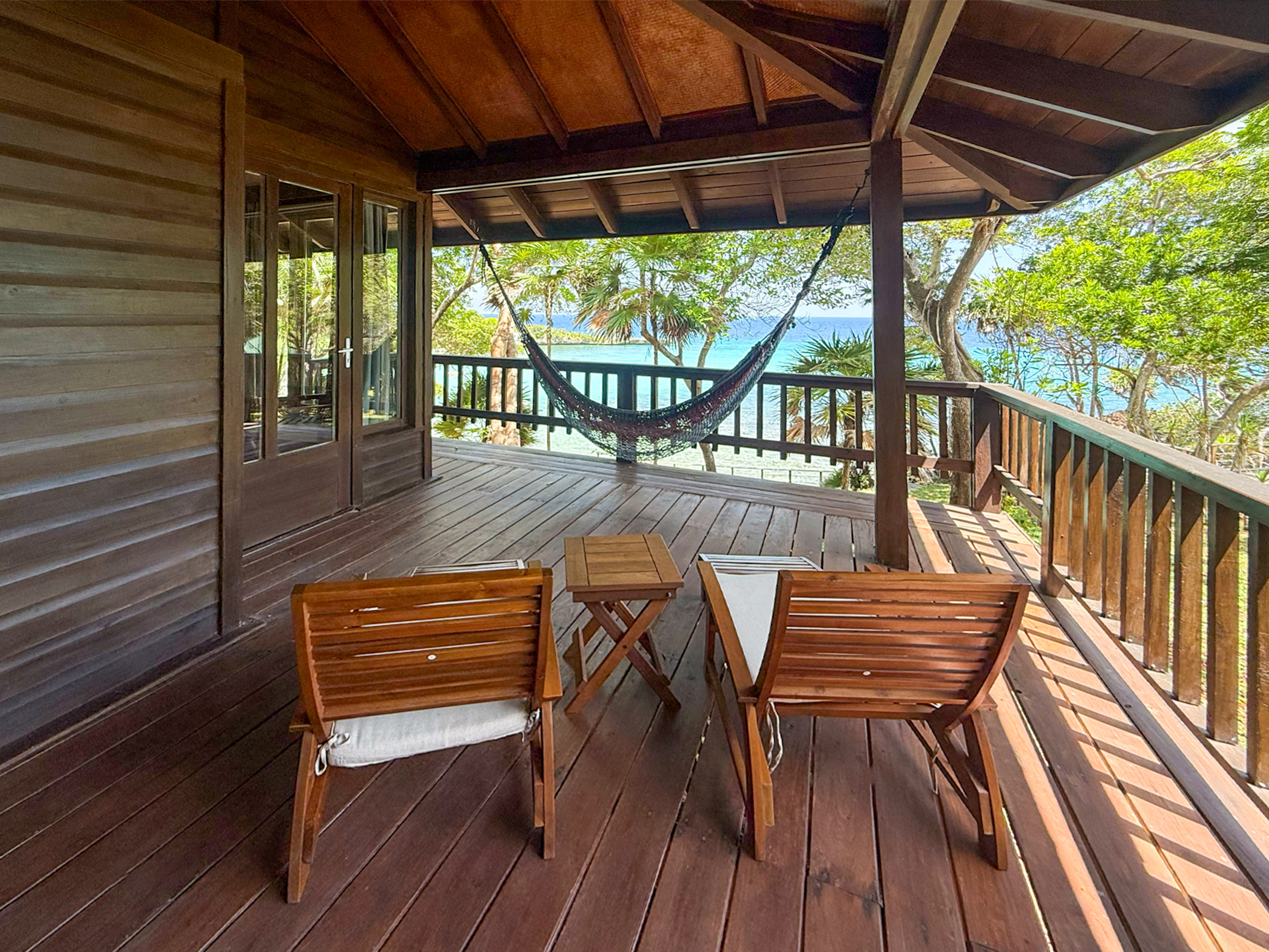 Oceanfront wooden deck with hammock, chairs, and tropical sea view.