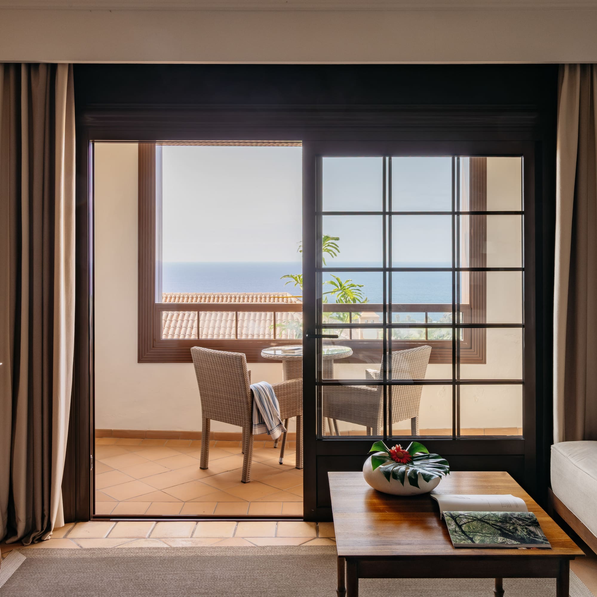 Hotel living room with ocean view balcony and patio seating.