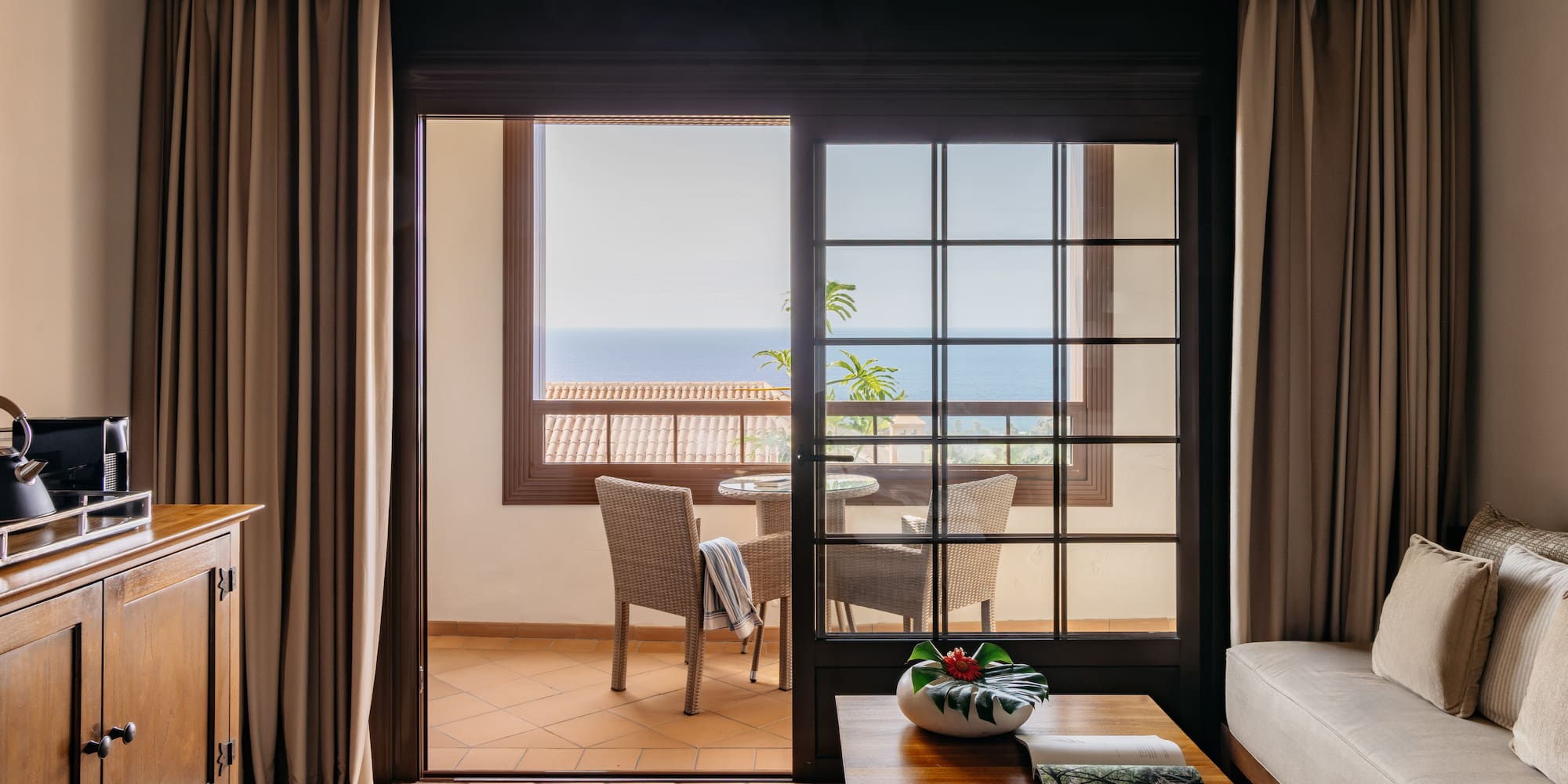 Hotel living room with ocean view balcony and patio seating.