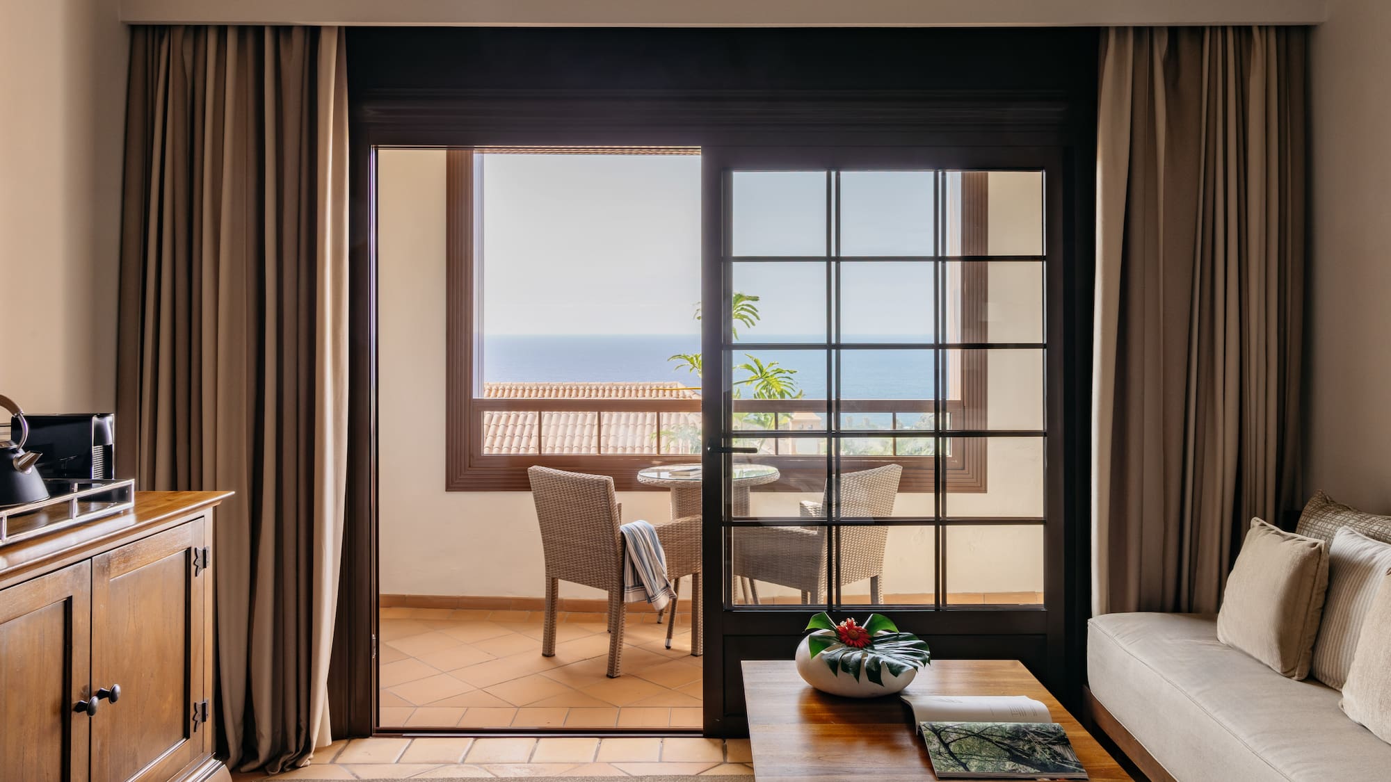 Hotel living room with ocean view balcony and patio seating.