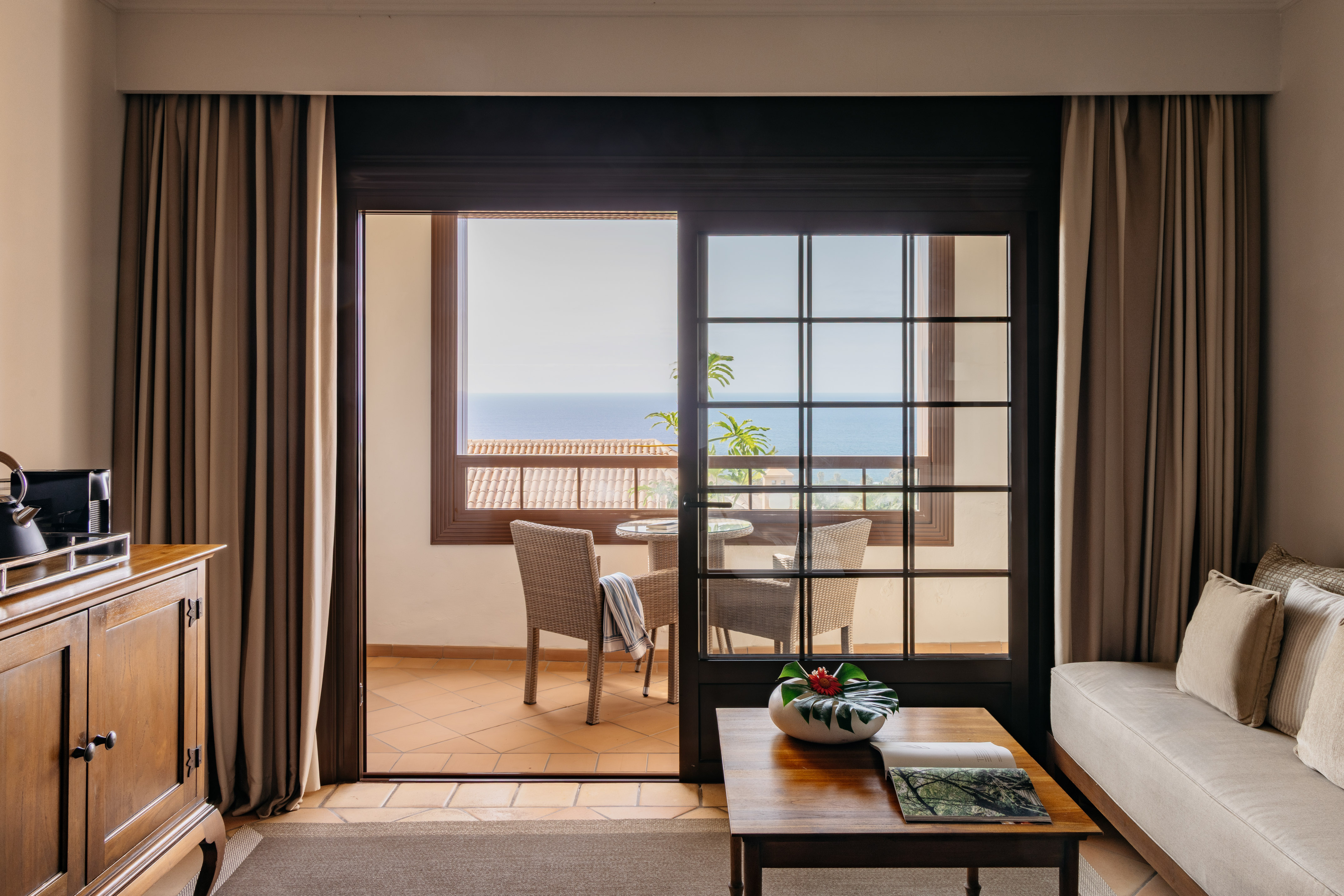 Hotel living room with ocean view balcony and patio seating.