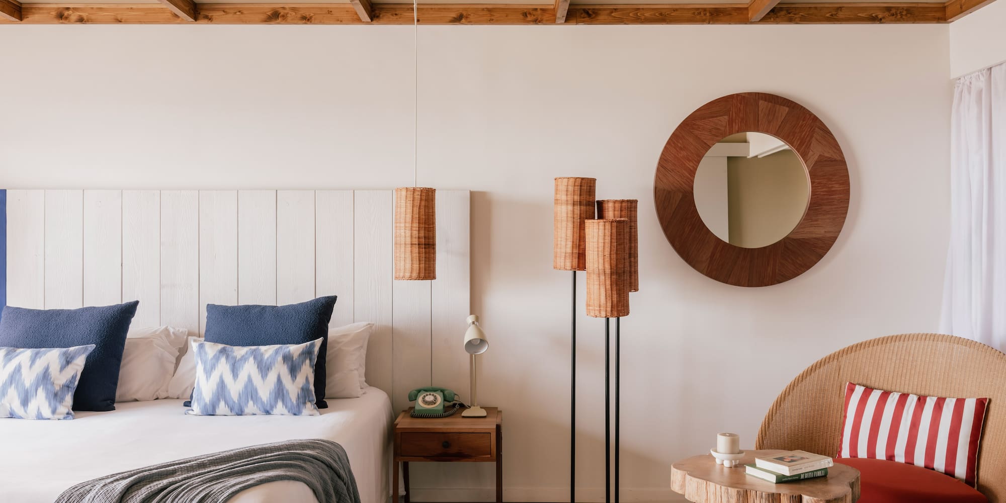 Coastal bohemian bedroom with white bed, blue pillows, wooden ceiling, wicker decor.