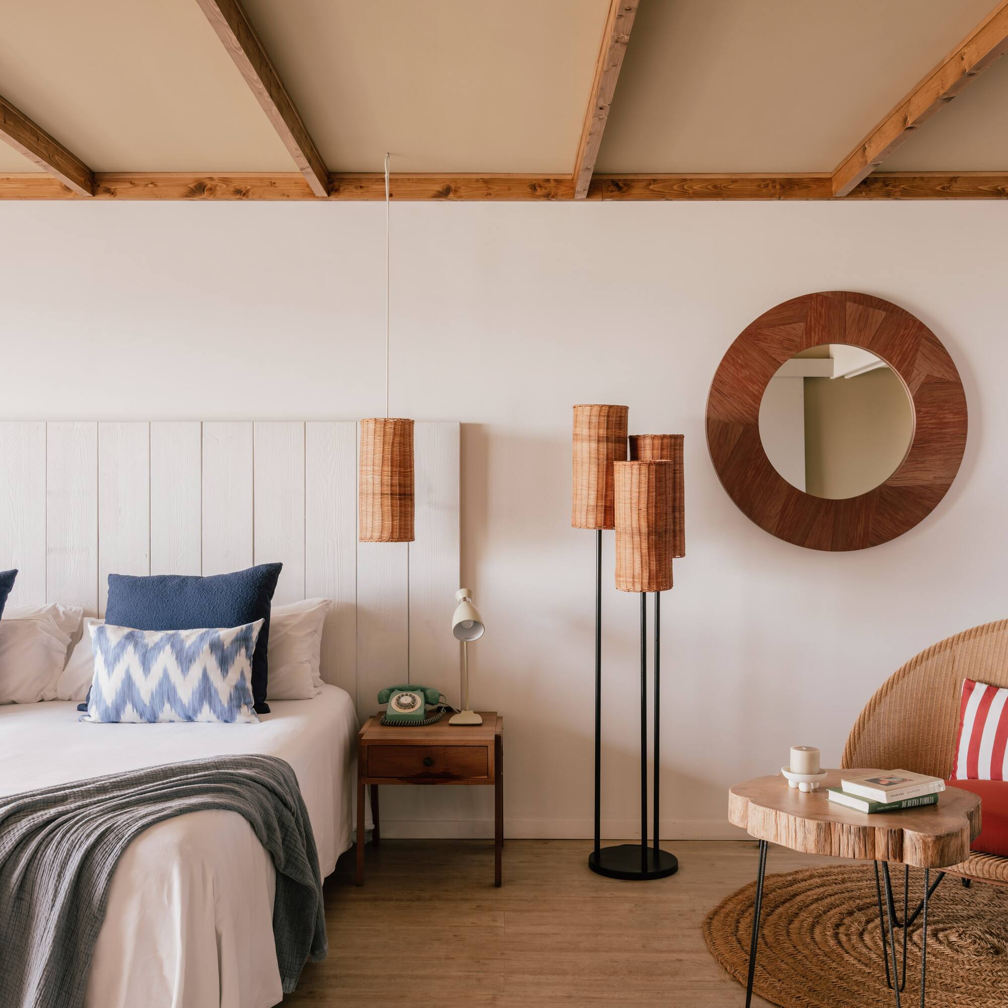 Cozy bedroom with white bed, blue pillows, wood ceiling, wicker chair, rattan lamps.