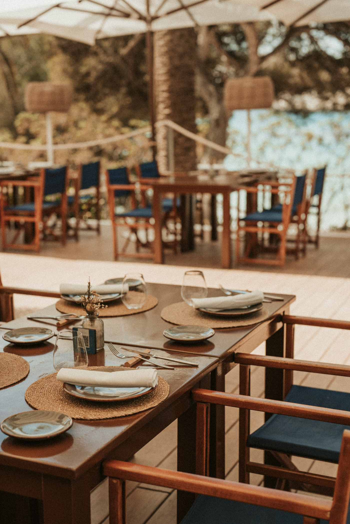 Al fresco dining table set with placemats and blue chairs on a restaurant patio.