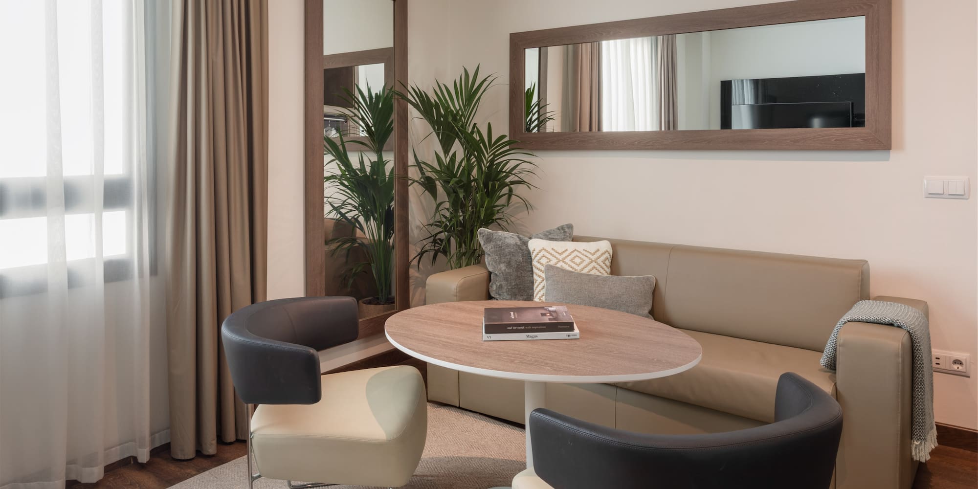 Modern living room with neutral sofa, round table, stylish chairs, and large mirrors.