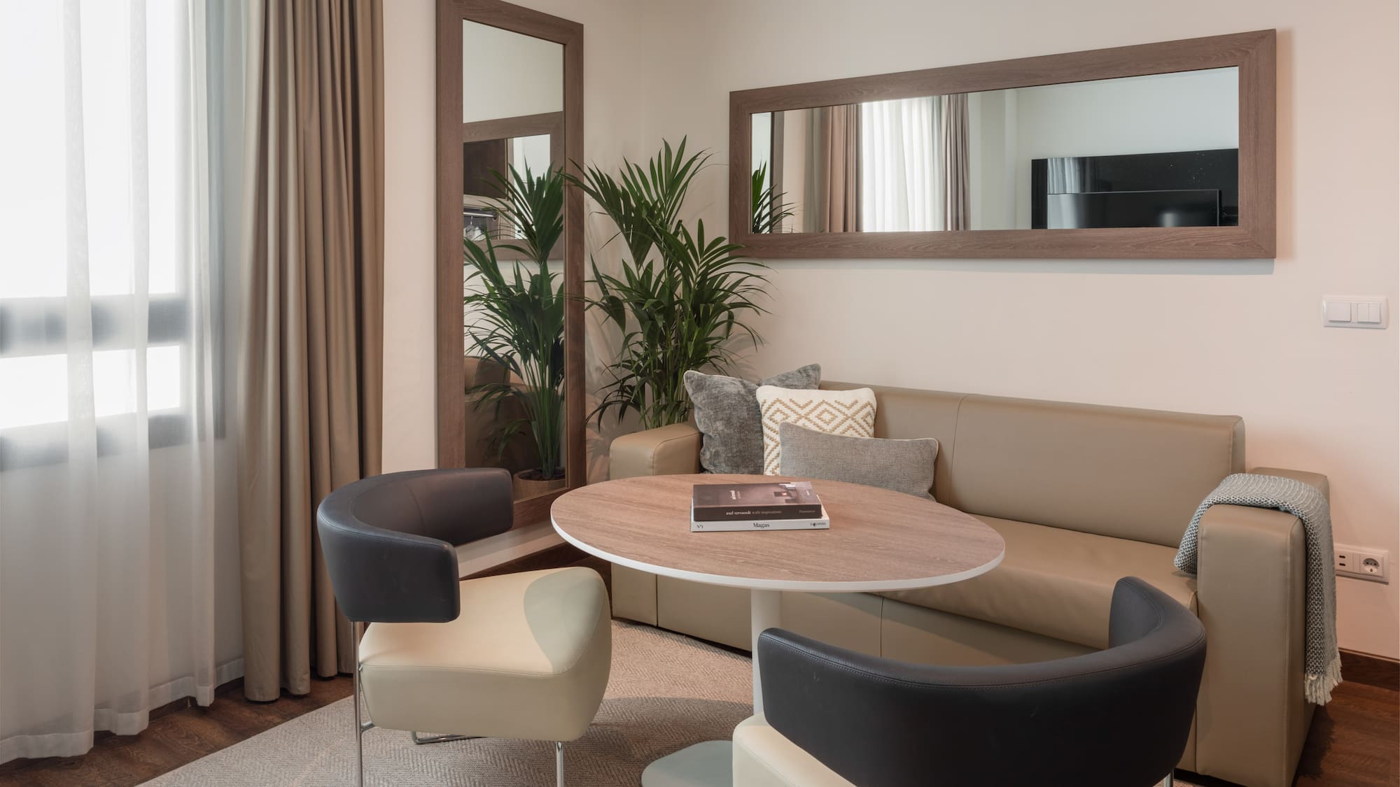 Modern living room with neutral sofa, round table, stylish chairs, and large mirrors.