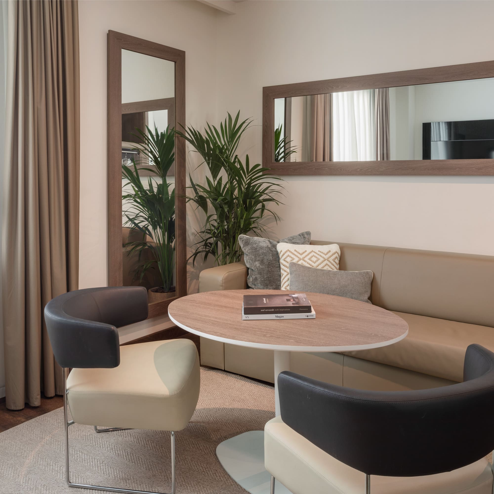 Modern living room with neutral sofa, round table, stylish chairs, and large mirrors.