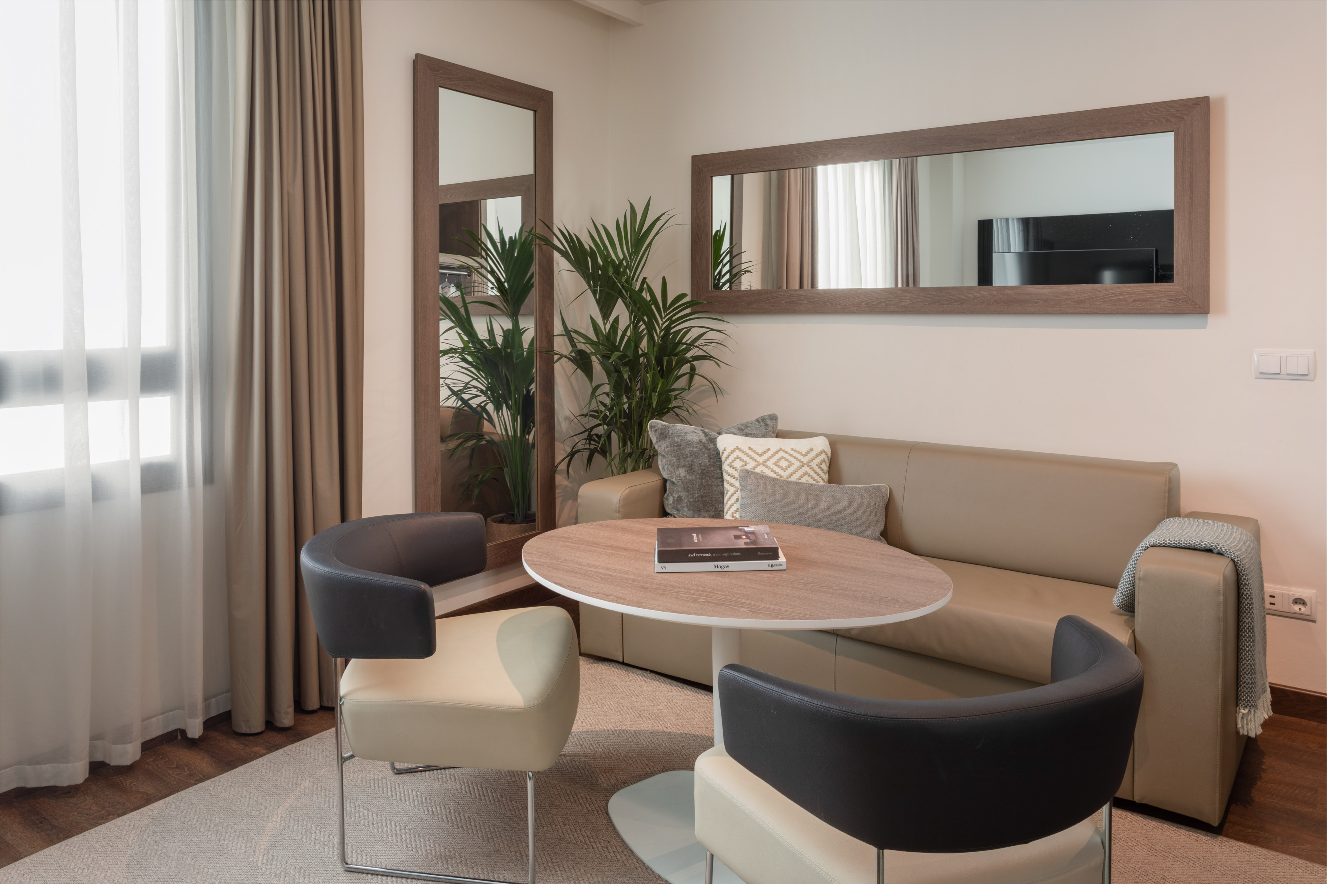 Modern living room with neutral sofa, round table, stylish chairs, and large mirrors.