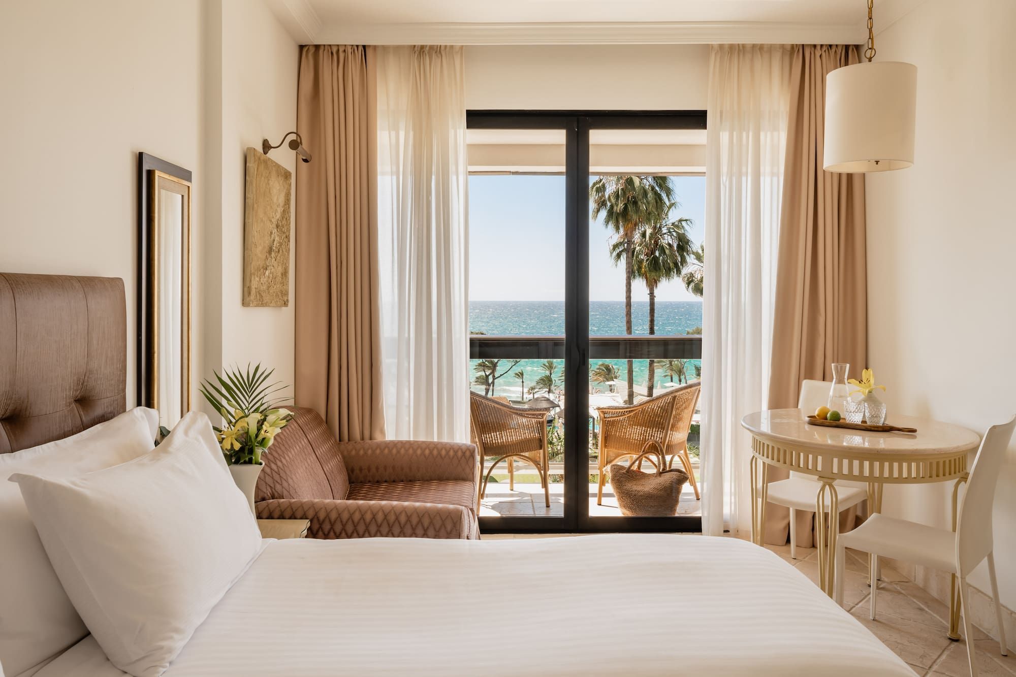 a room with a bed and chairs and a table and chairs and a balcony with a view of the ocean