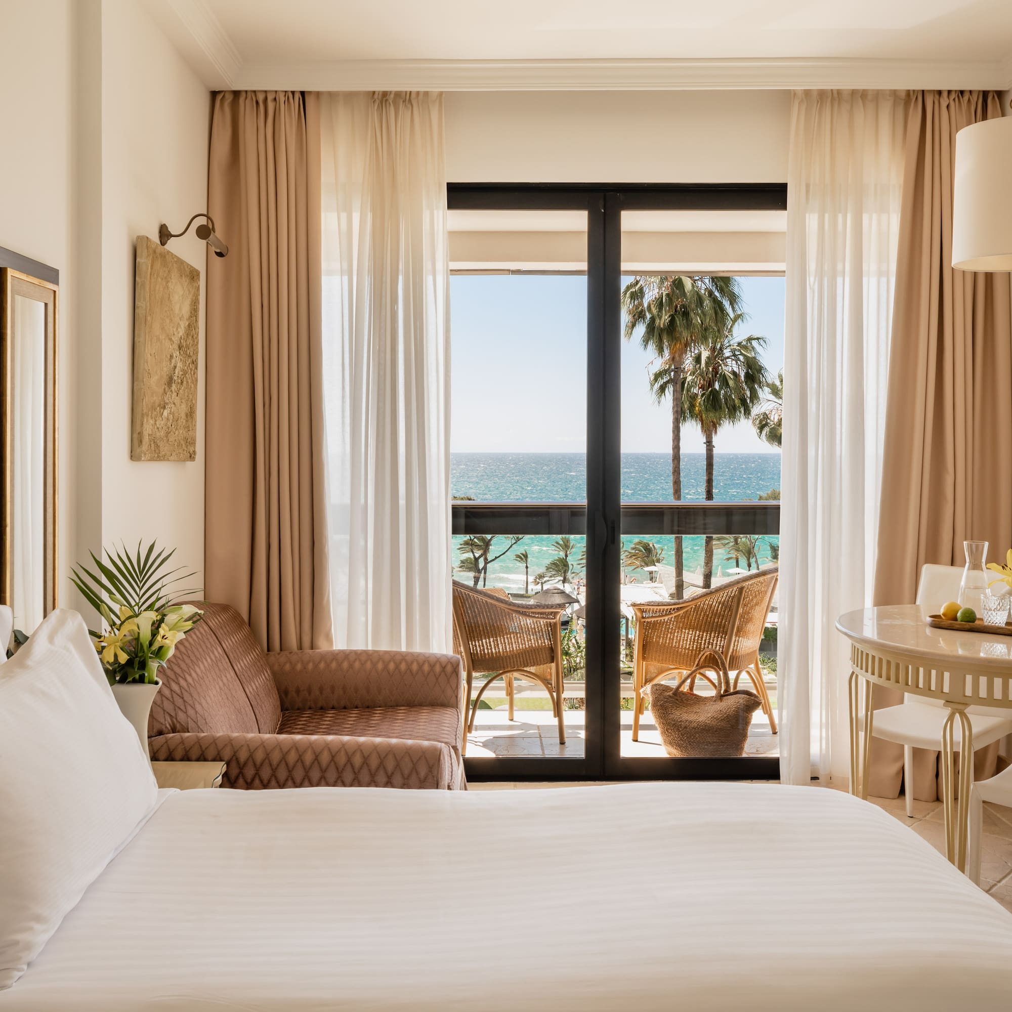 a room with a bed and chairs and a table and chairs and a balcony with a view of the ocean