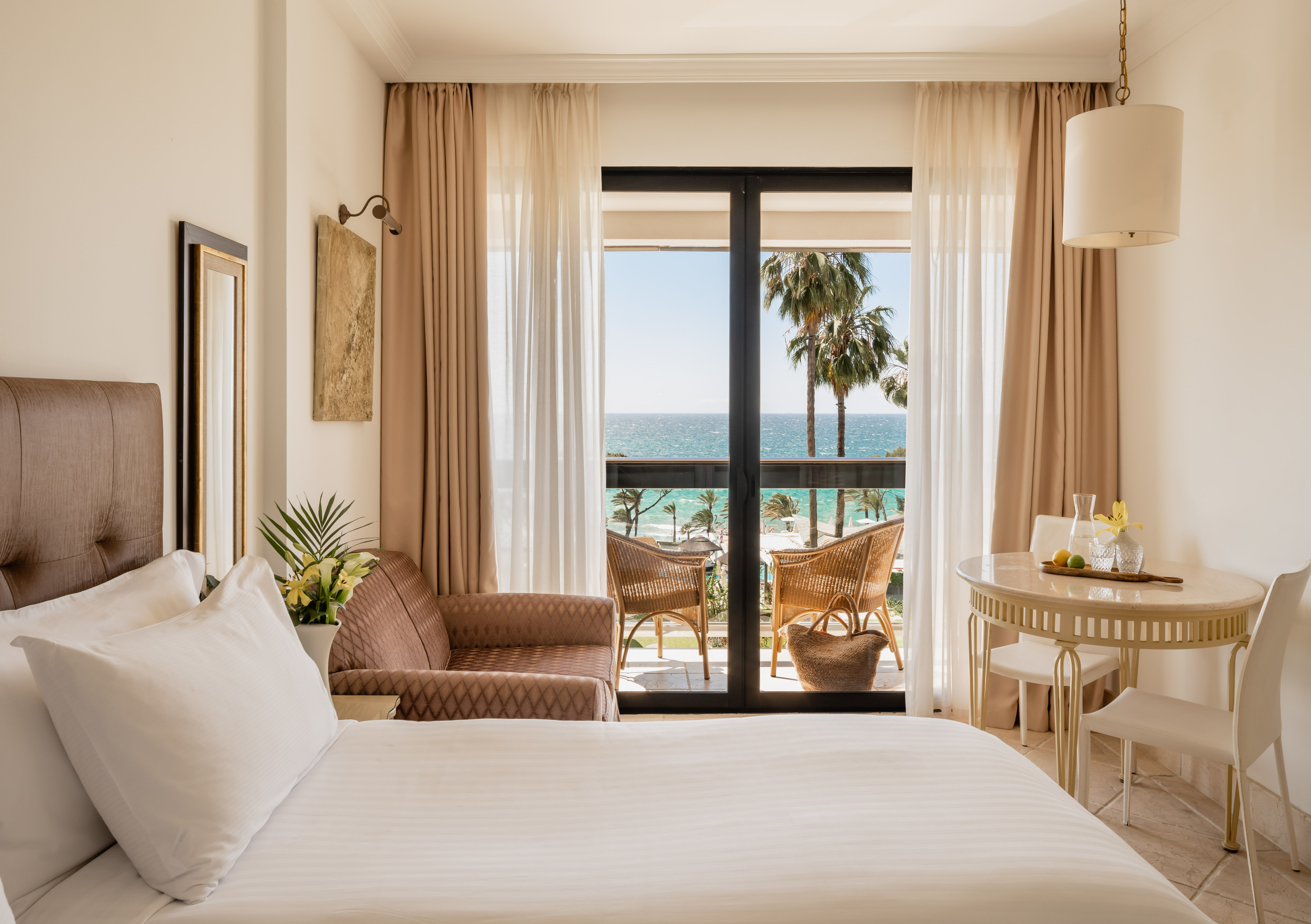 a room with a bed and chairs and a table and chairs and a balcony with a view of the ocean