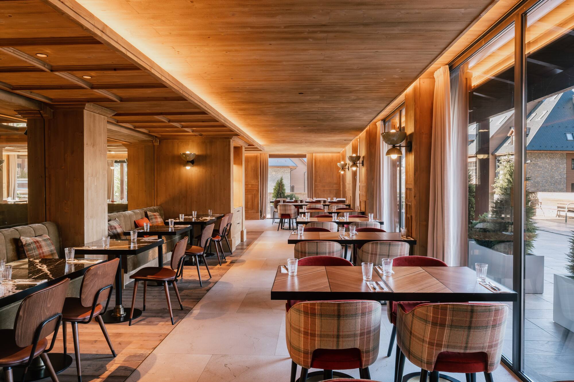 Comedor de madera moderno, mesas preparadas, sillas de diseño, ventanales.