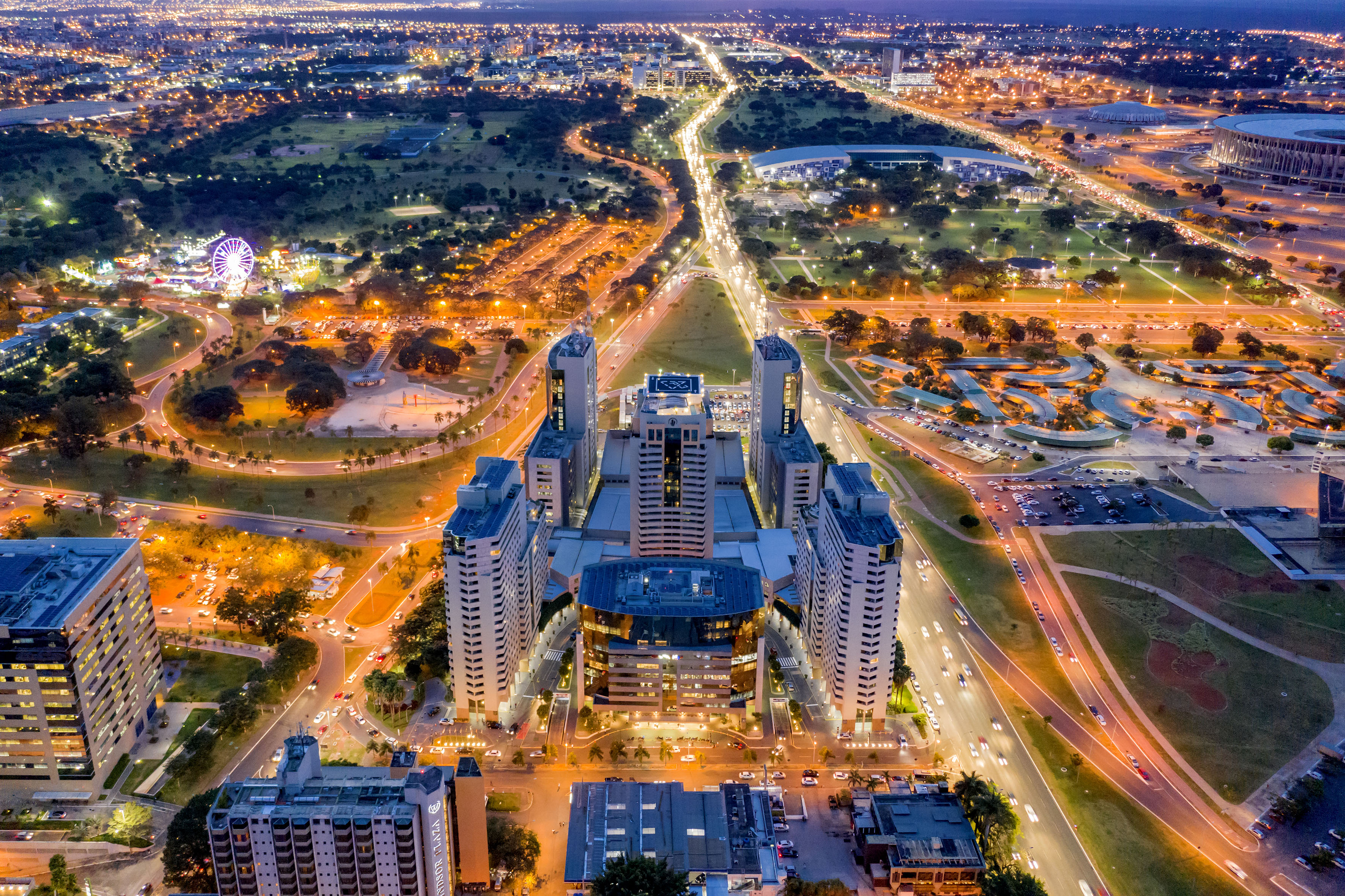 Aerial night cityscape: illuminated buildings, roads, traffic, and a bright Ferris wheel.