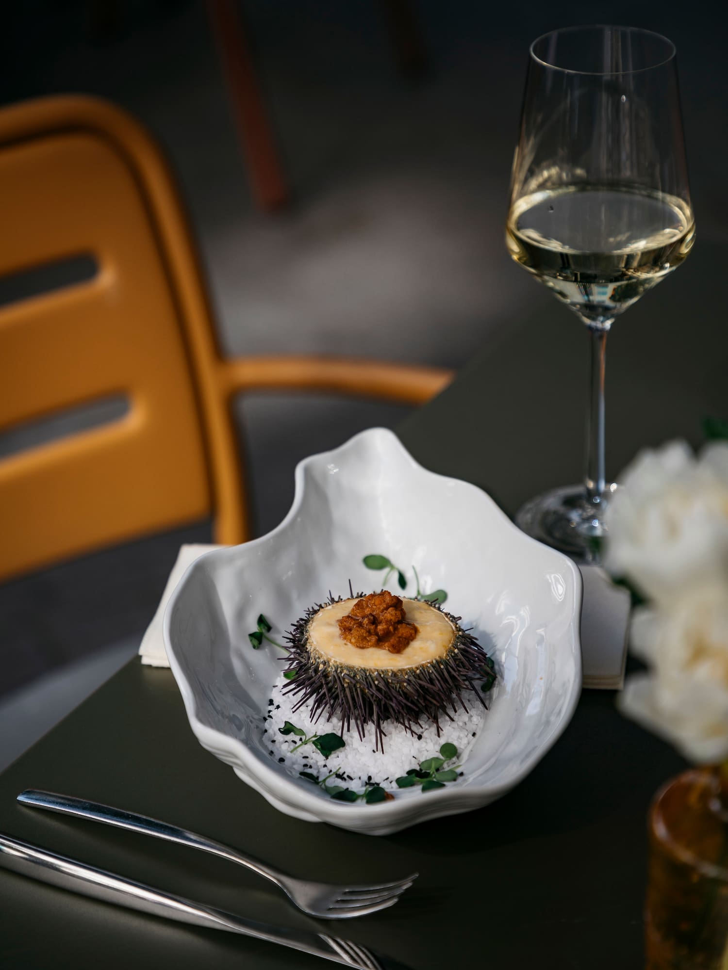 a sea urchin in a white bowl next to a glass of wine