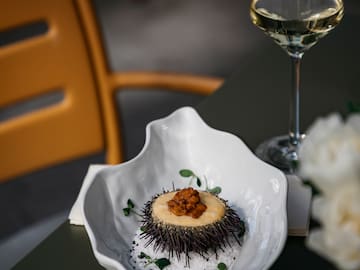 a sea urchin in a white bowl next to a glass of wine