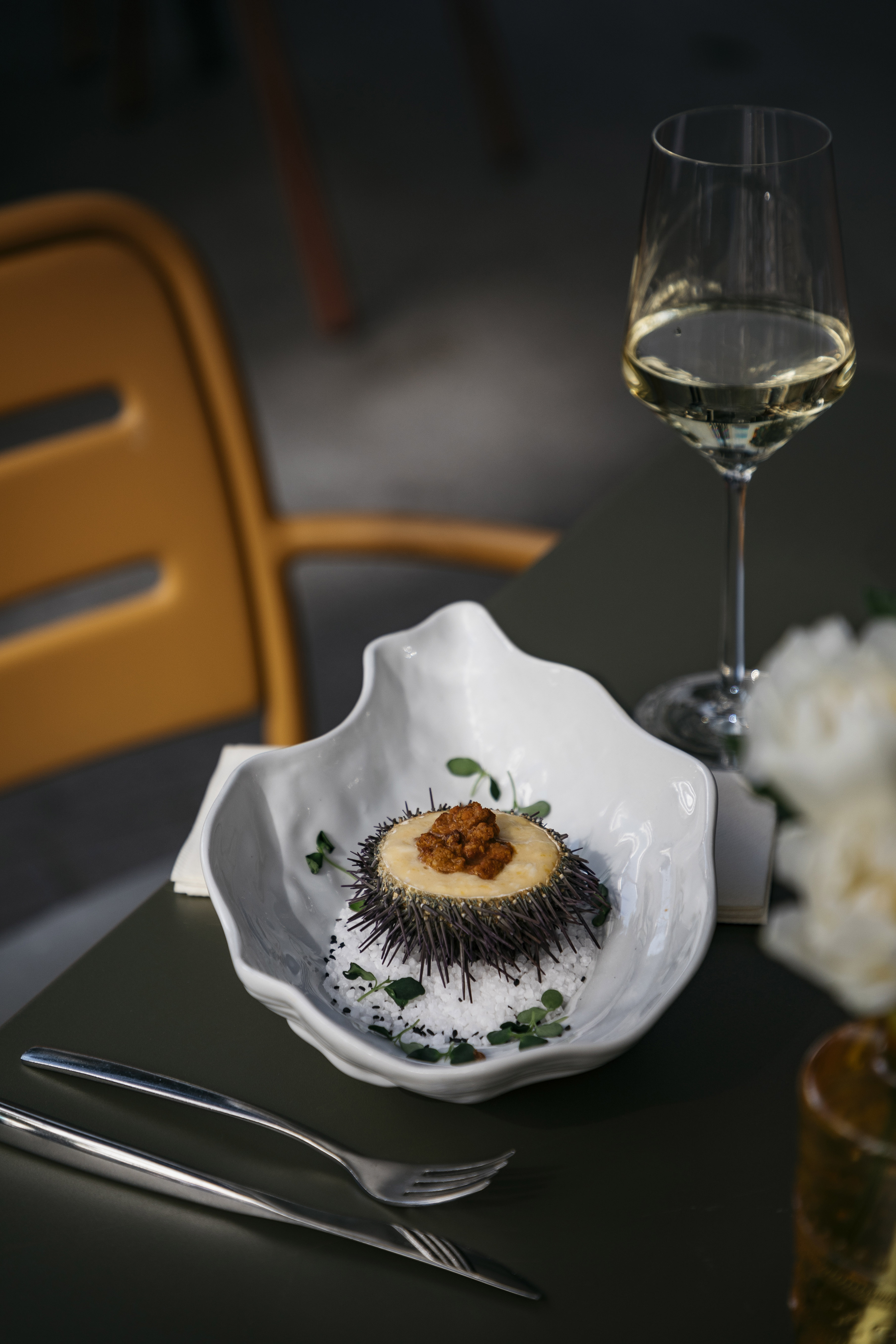 a sea urchin in a white bowl next to a glass of wine