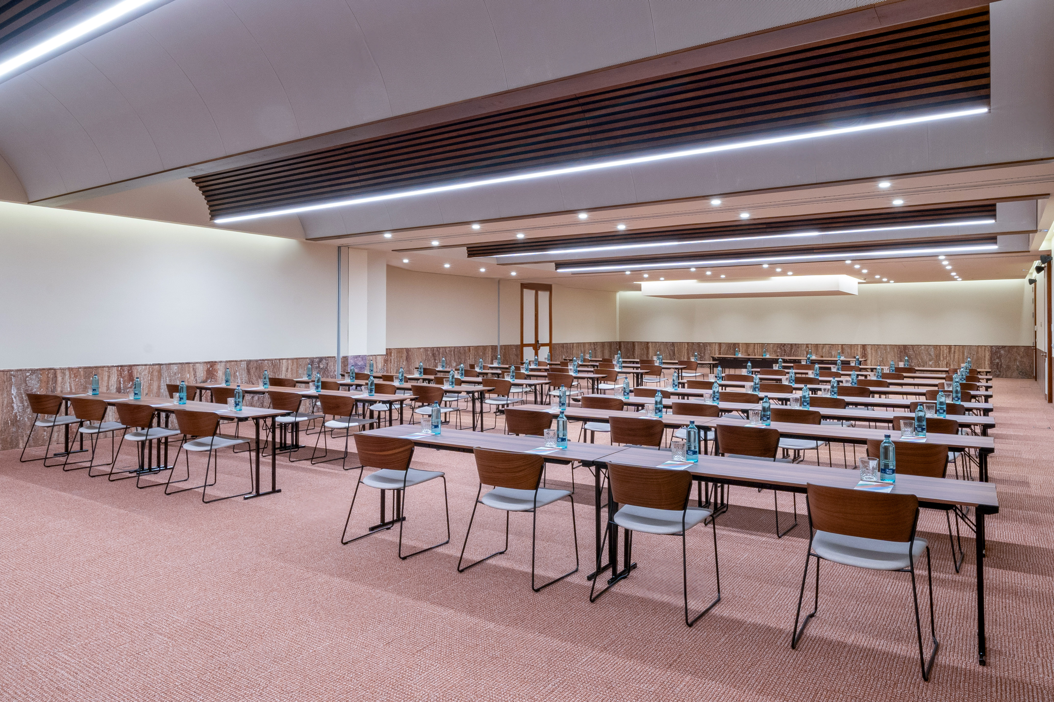 Modern empty conference room with rows of tables, chairs, and bottled water.