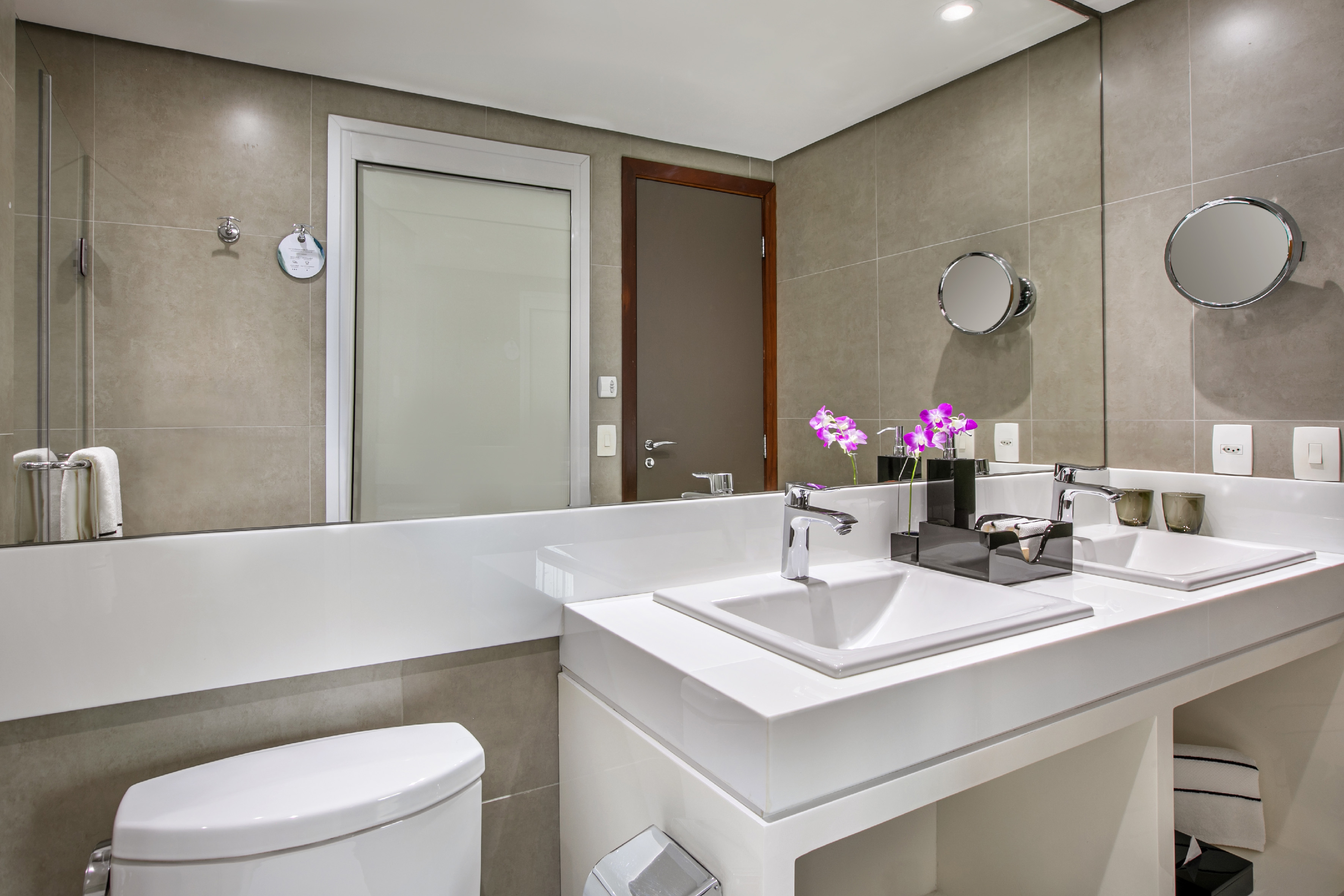 Modern bathroom with white double vanity, chrome fixtures, and purple orchids.