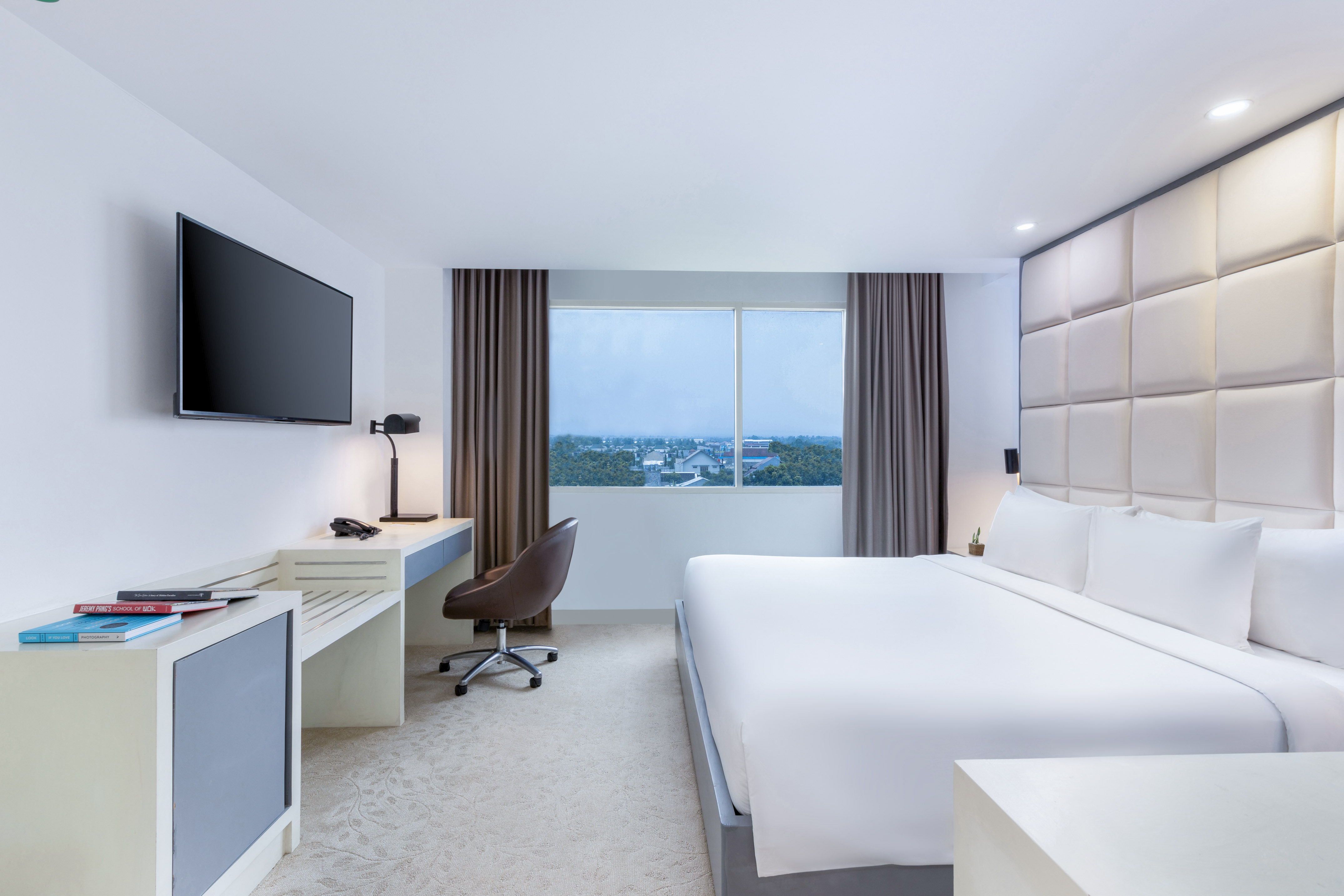 Modern hotel room with king bed, desk, wall-mounted TV, and window city view.