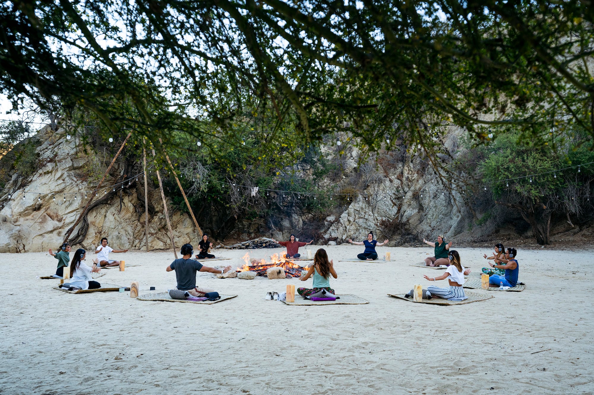 a group of people sitting on mats in a circle with a fire