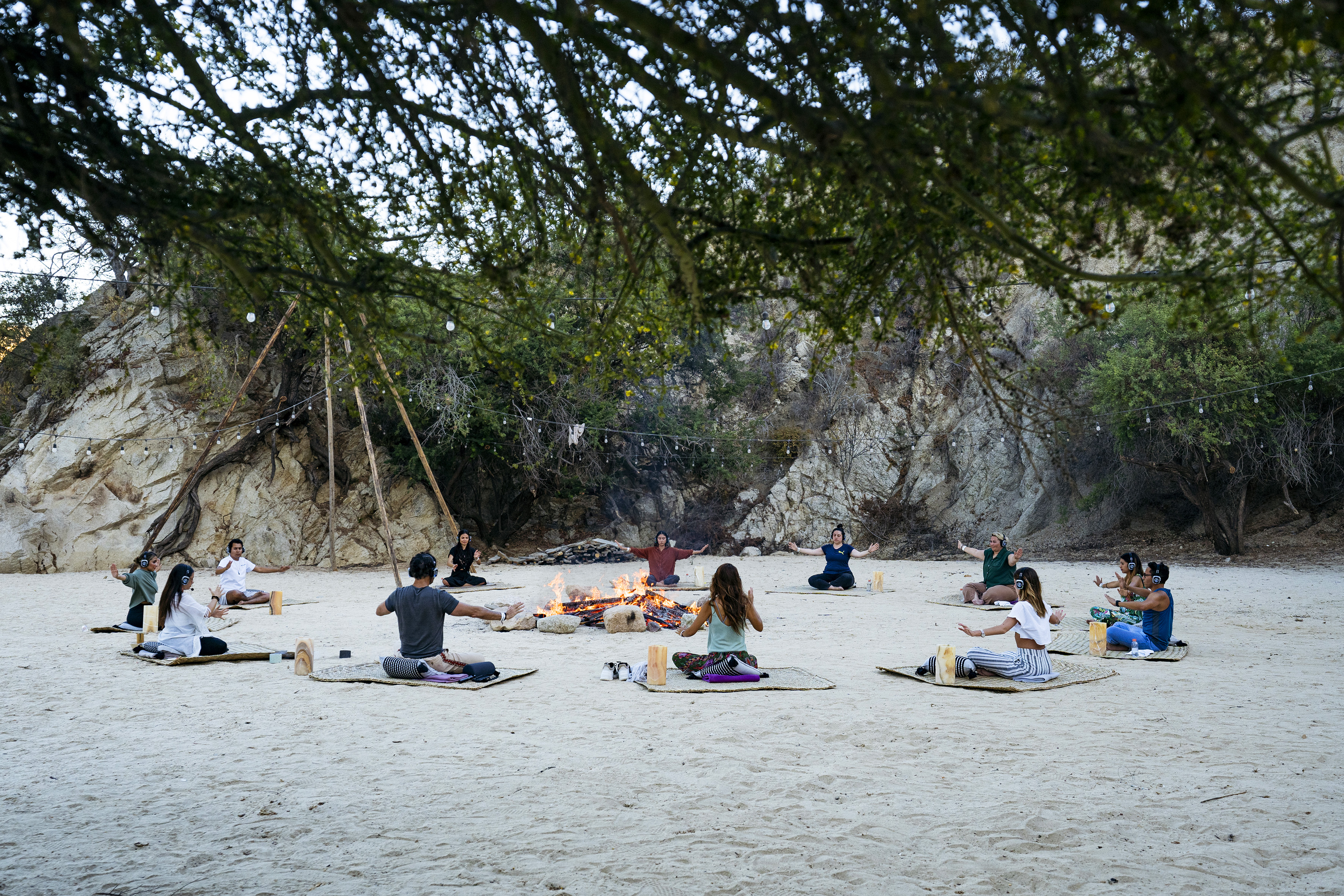 a group of people sitting on mats in a circle with a fire